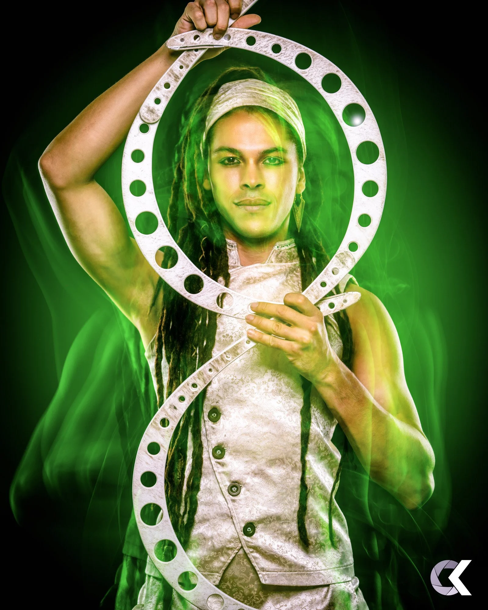 A woman with dreadlocks and a headband holding a metallic hoop with green light and smoke effects, wearing a textured sleeveless top.