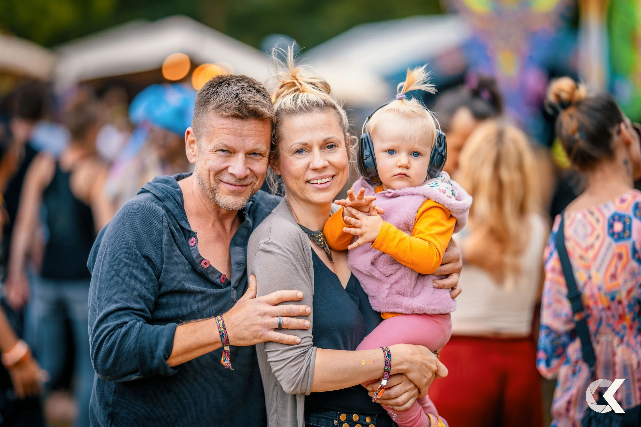 A happy family at an outdoor event, with a man, a woman, and a young girl, surrounded by a crowd of people.