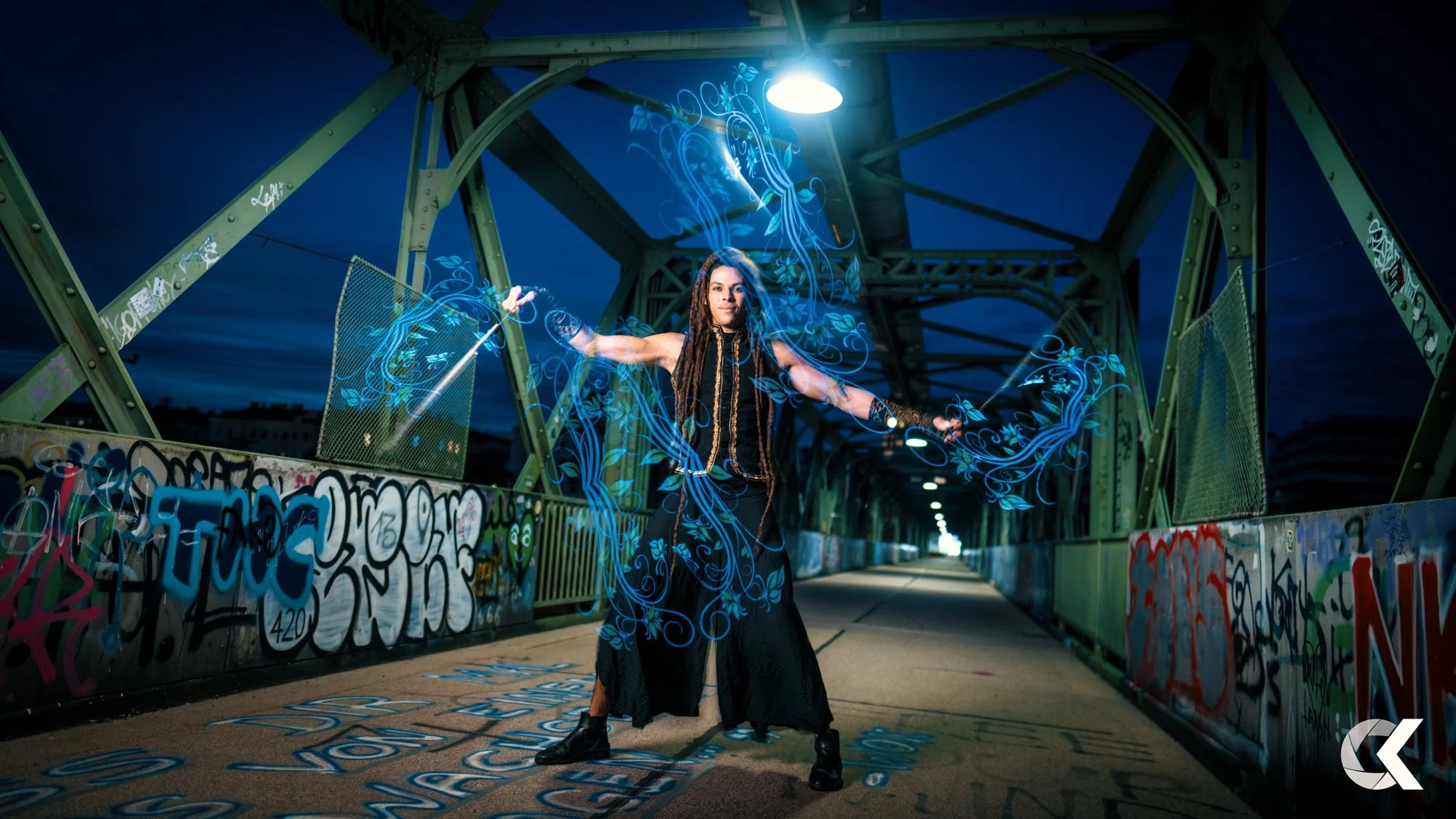 A woman with long dreadlocks dressed in black standing with arms outstretched on a graffiti-covered bridge at night, with blue glowing digital patterns emanating from her hands.