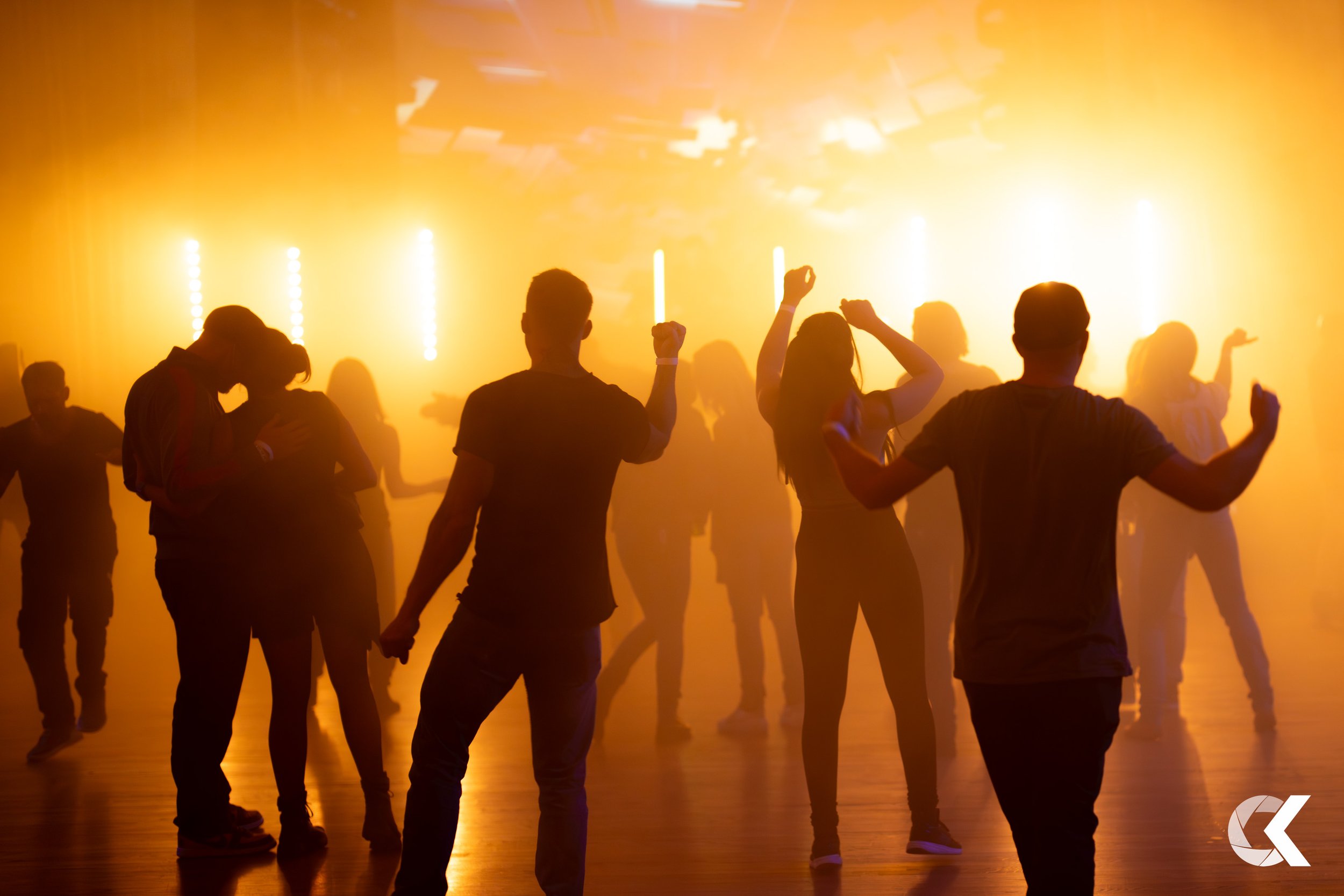People dancing and socializing in a dimly lit nightclub with yellow-orange lighting, silhouette effect.