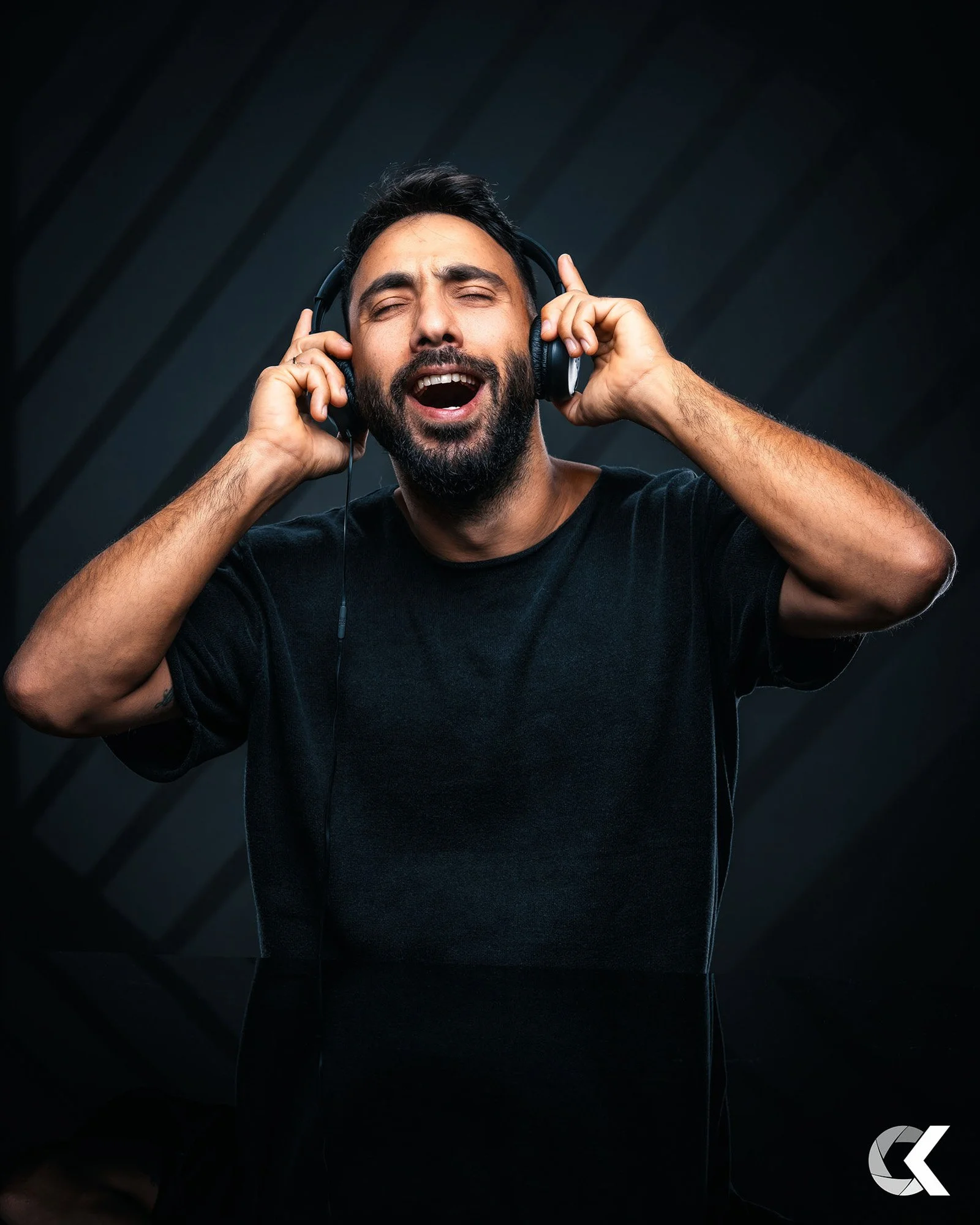 A man singing with his eyes closed, wearing headphones, in a dark studio setting.