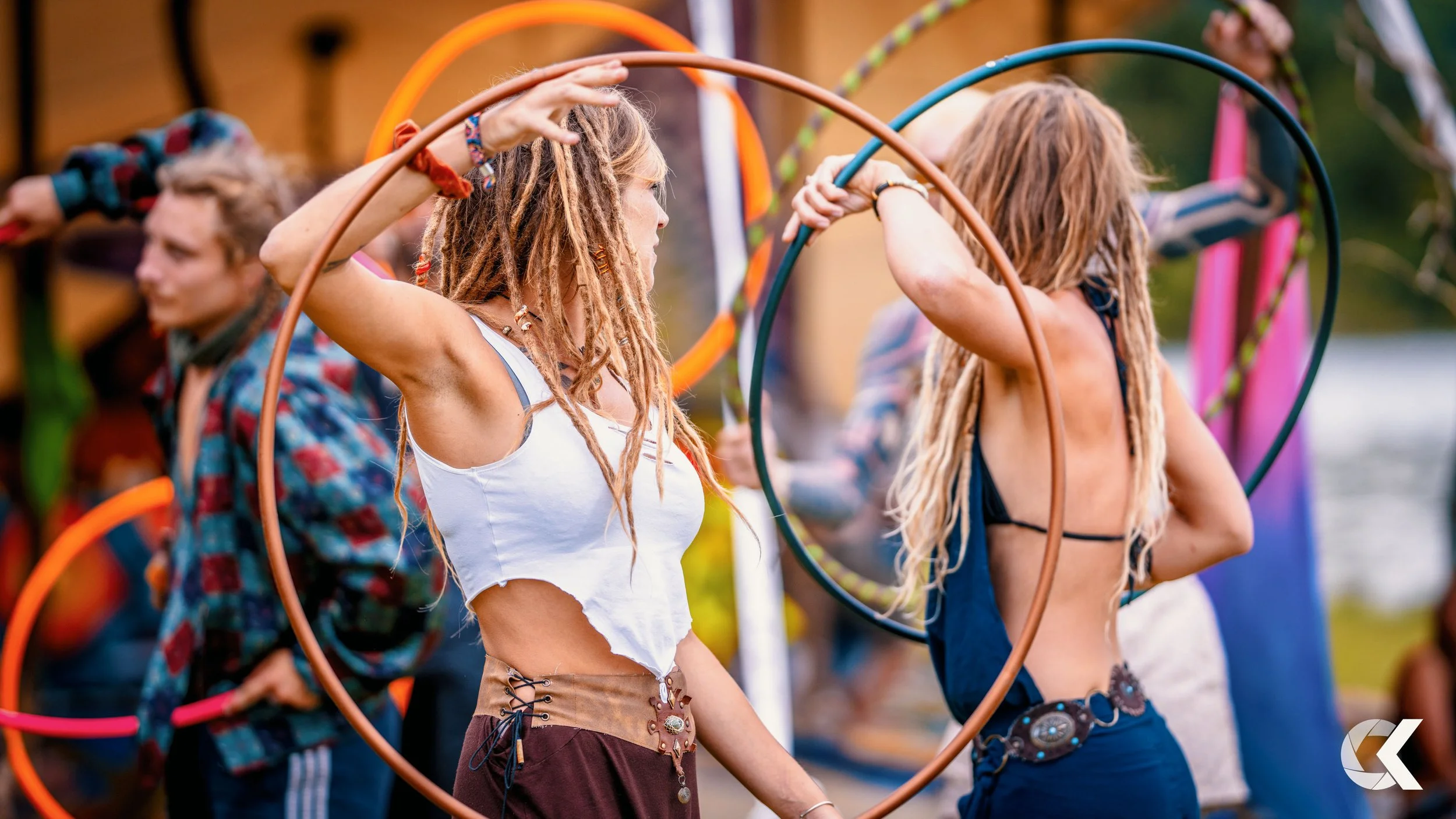 Multiple people, including two women with dreadlocks, are holding hula hoops during a festival or outdoor gathering.