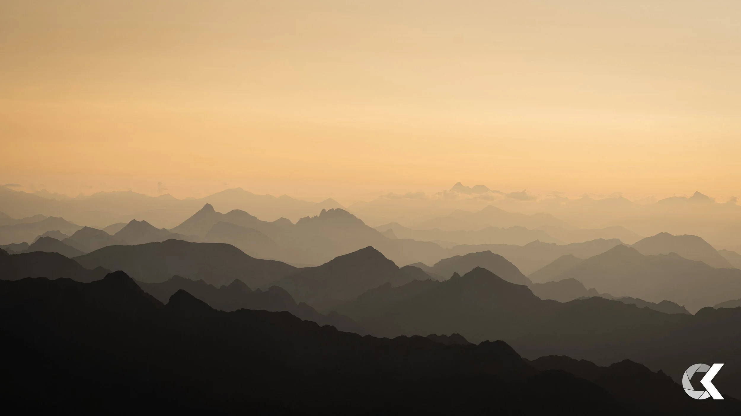 Layered mountain silhouette at sunrise or sunset with a soft, peach-colored sky.