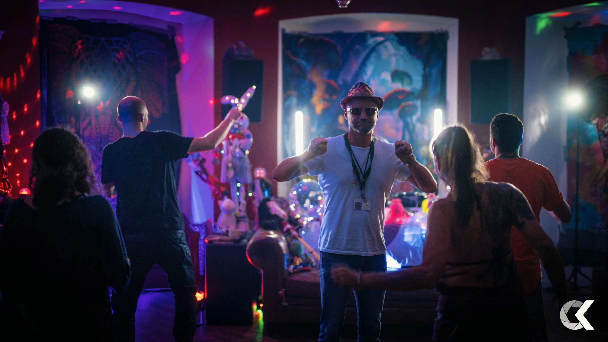 People dancing and enjoying party in a colorful room with neon and abstract art decorations.
