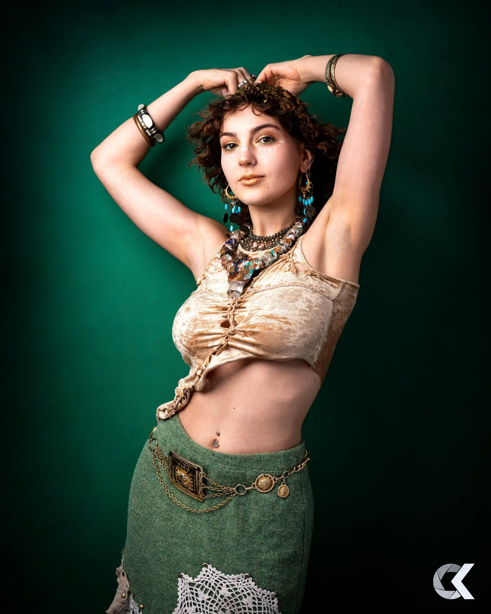 Young woman with curly hair and jewelry posing against a green background