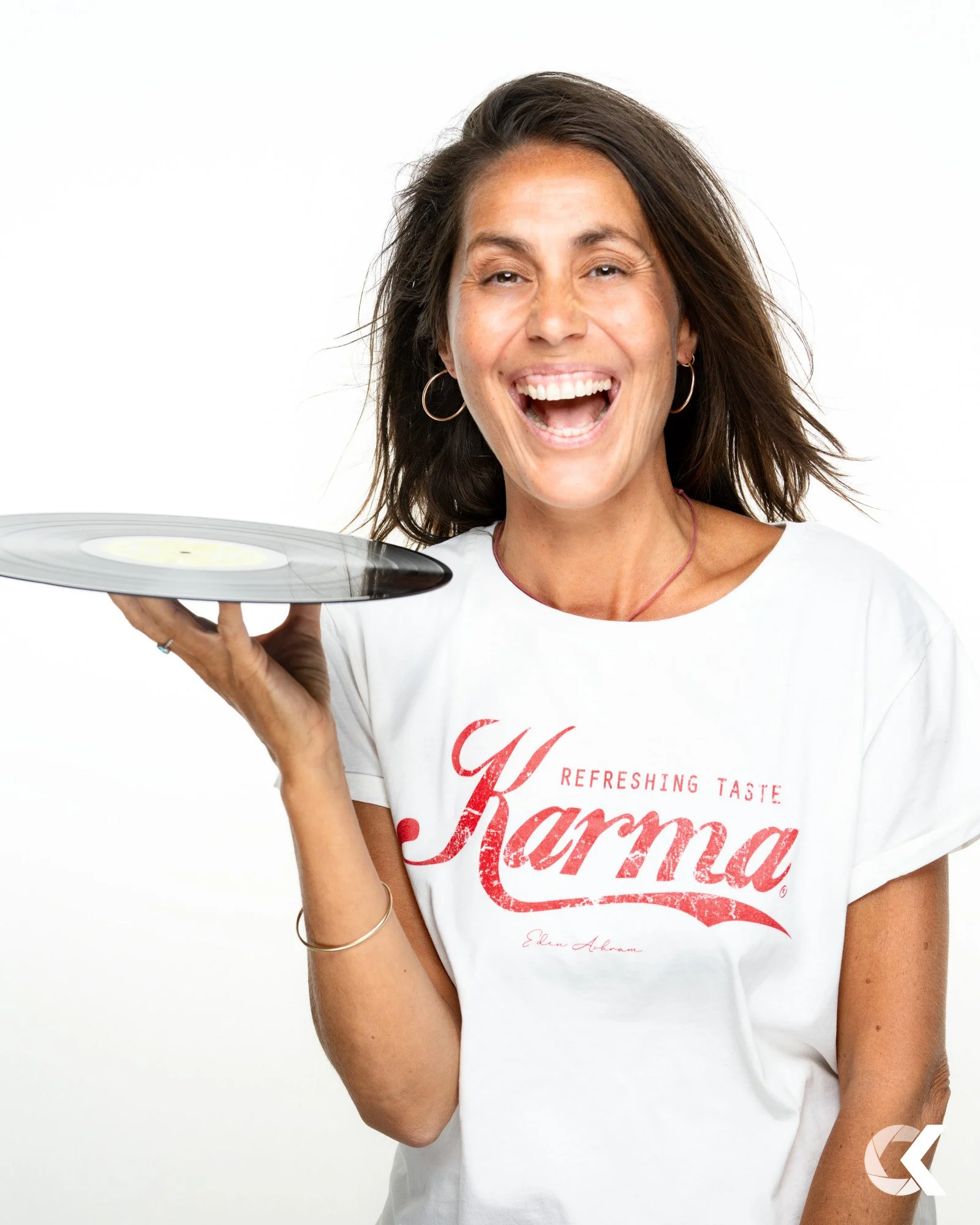 Lächelnde Frau mit Ohrringen hält einen Schallplattenspieler und trägt ein weißes T-Shirt mit rotem Text 'Karma'