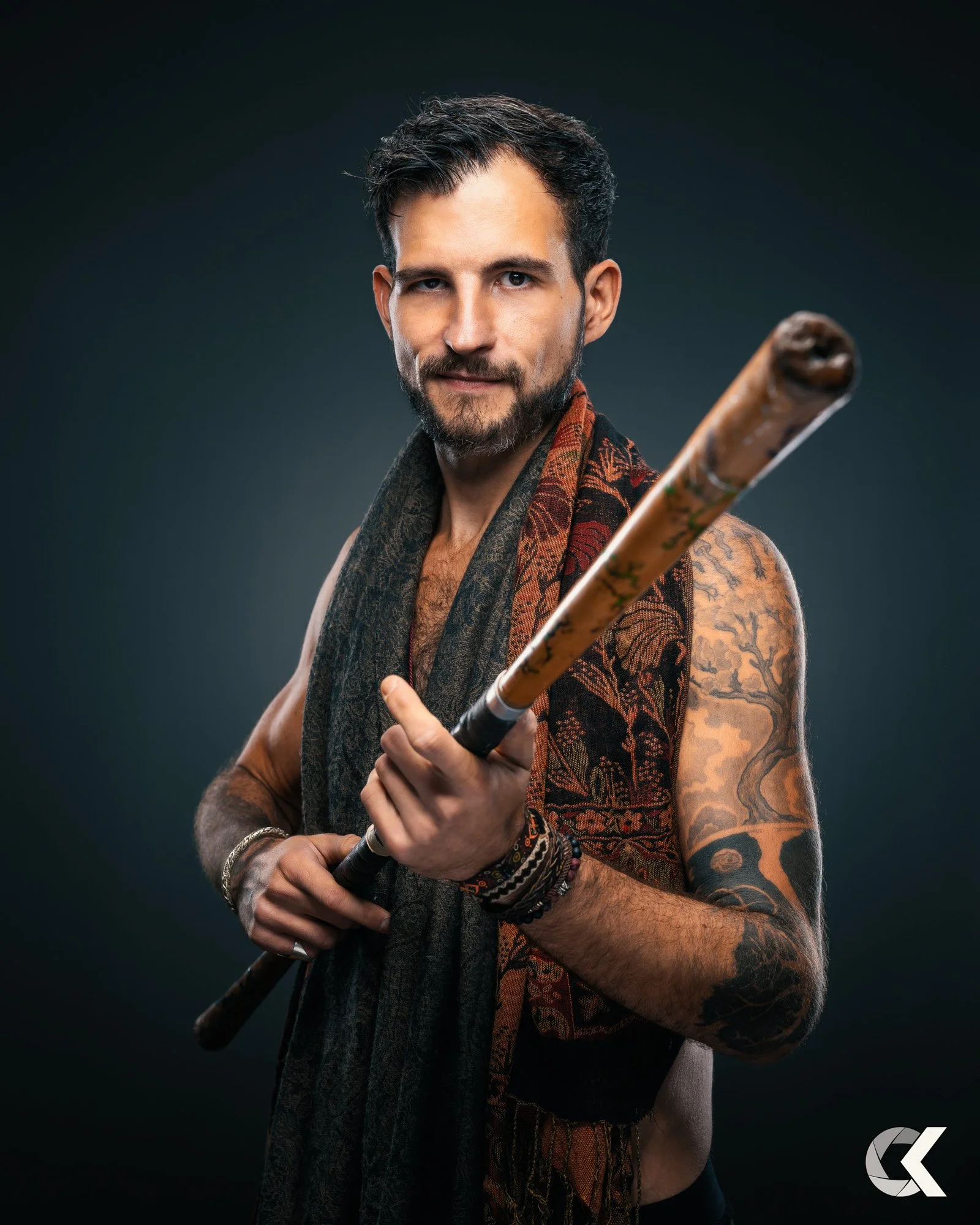 Ein Mann mit dunklem Haar, Bart und Tattoos, der in die Kamera schaut und einen Baseballschläger hält.