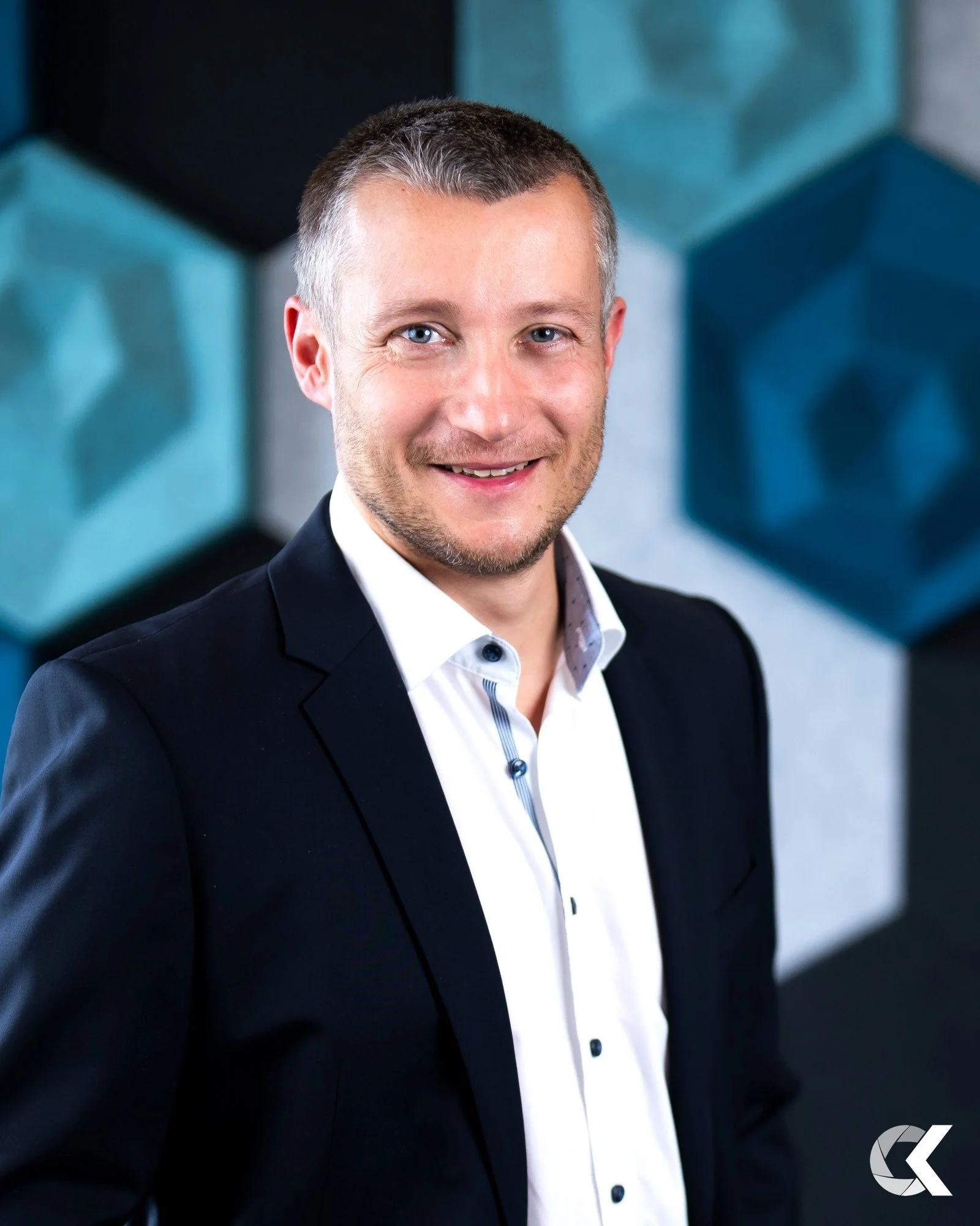 Professional man in a suit smiling for the camera, standing in front of a modern geometric art background.
