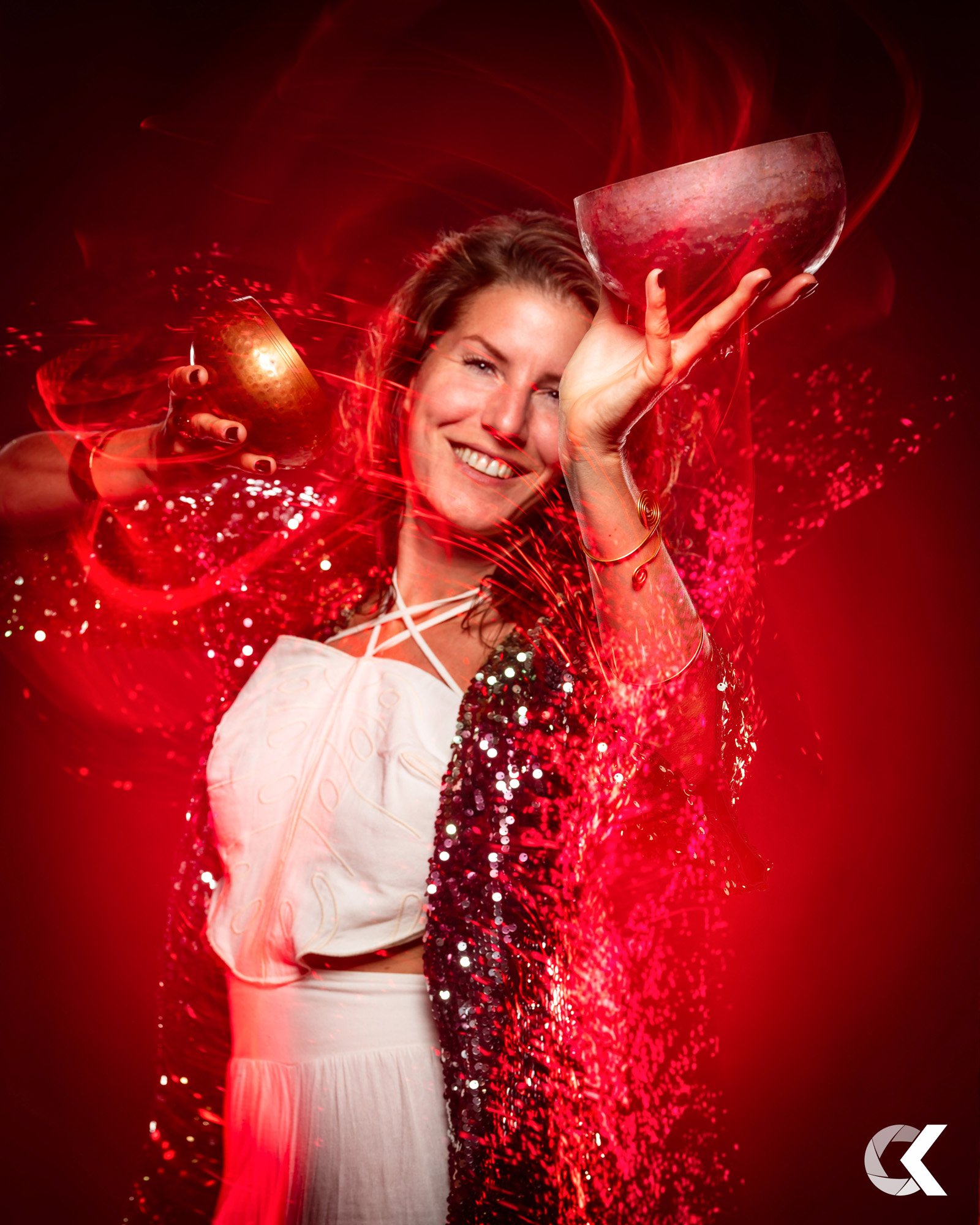A woman smiling and holding crystal bowls with a red and glittery background.