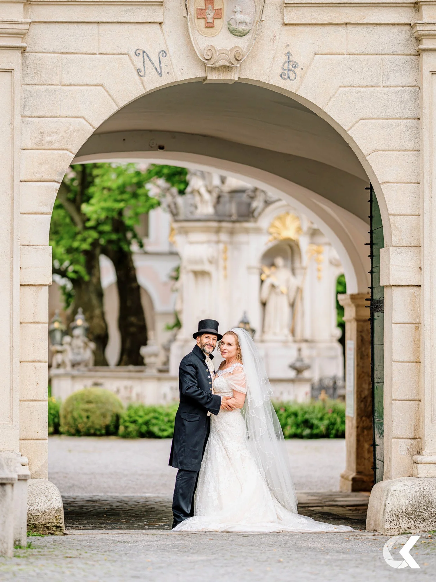 A bride and groom standing together under an archway in a historic European-style courtyard during their wedding.