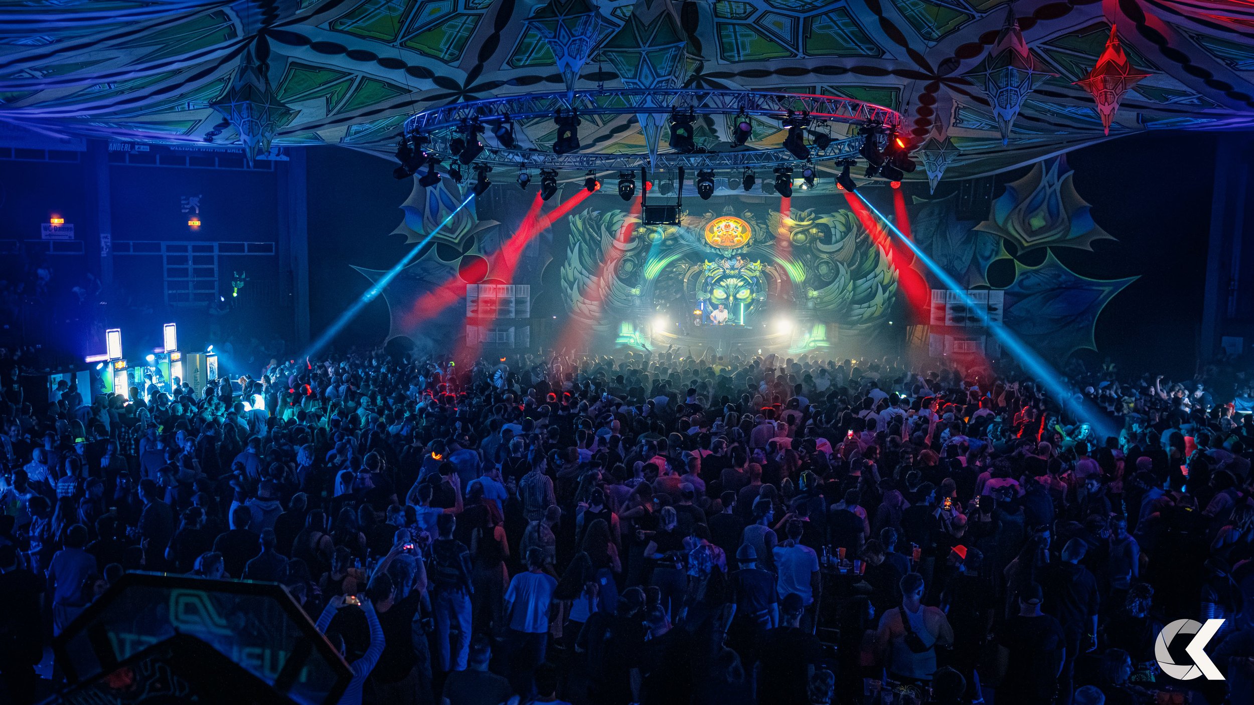 A large crowd of people at a concert or music festival with colorful lights and a decorated stage.