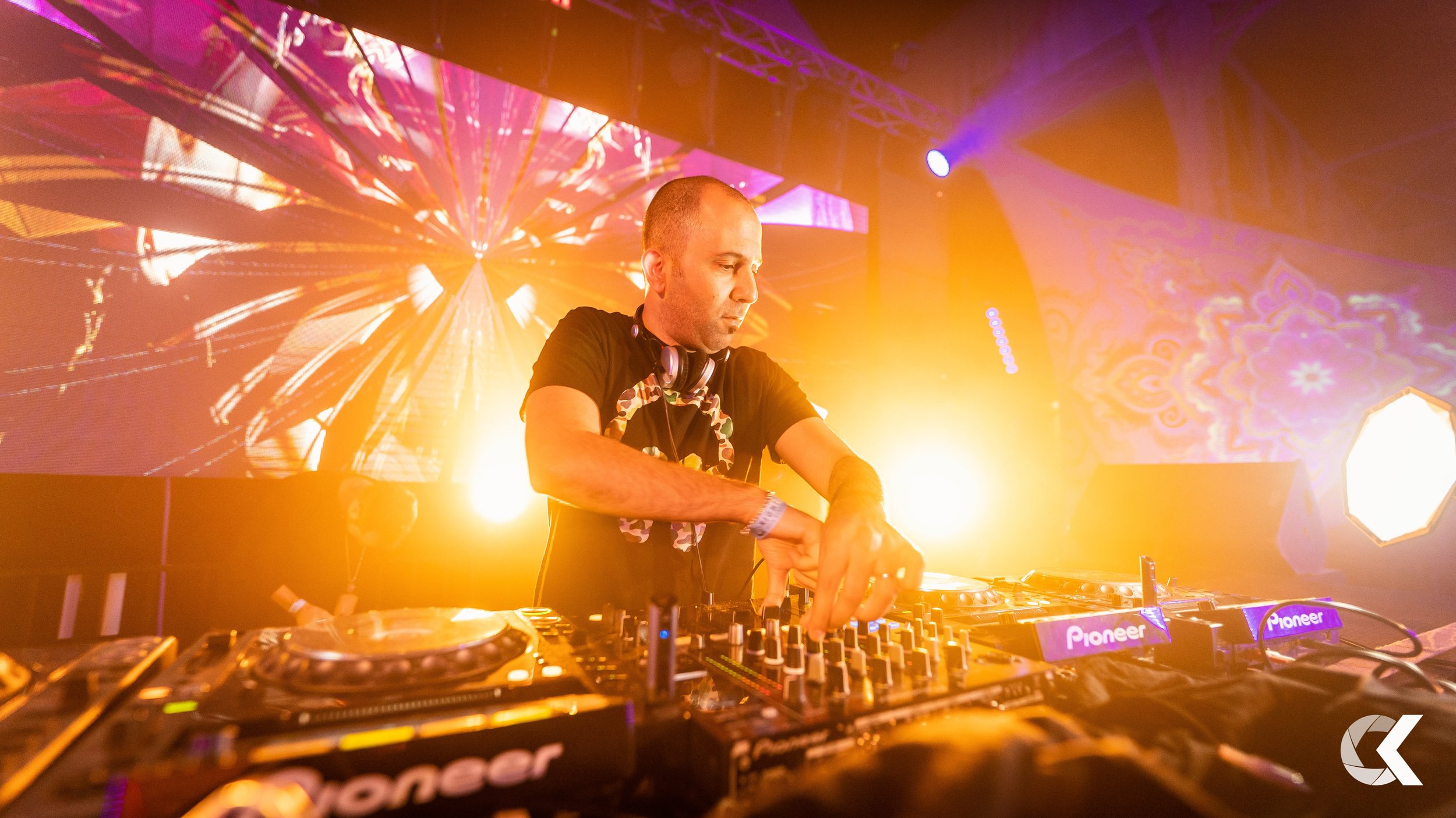 A DJ performing at a concert with vibrant lighting and colorful background visuals.