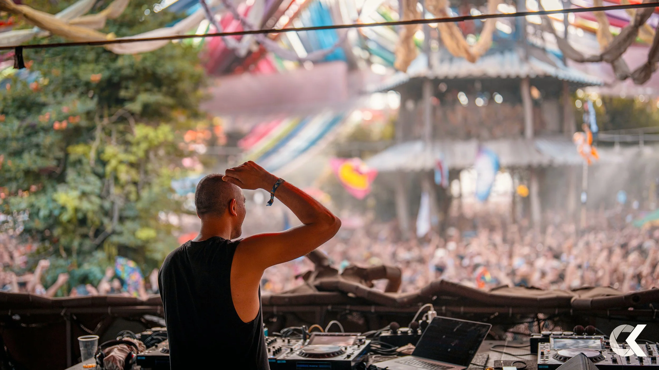 DJ performing at an outdoor music festival with a large crowd in the background.