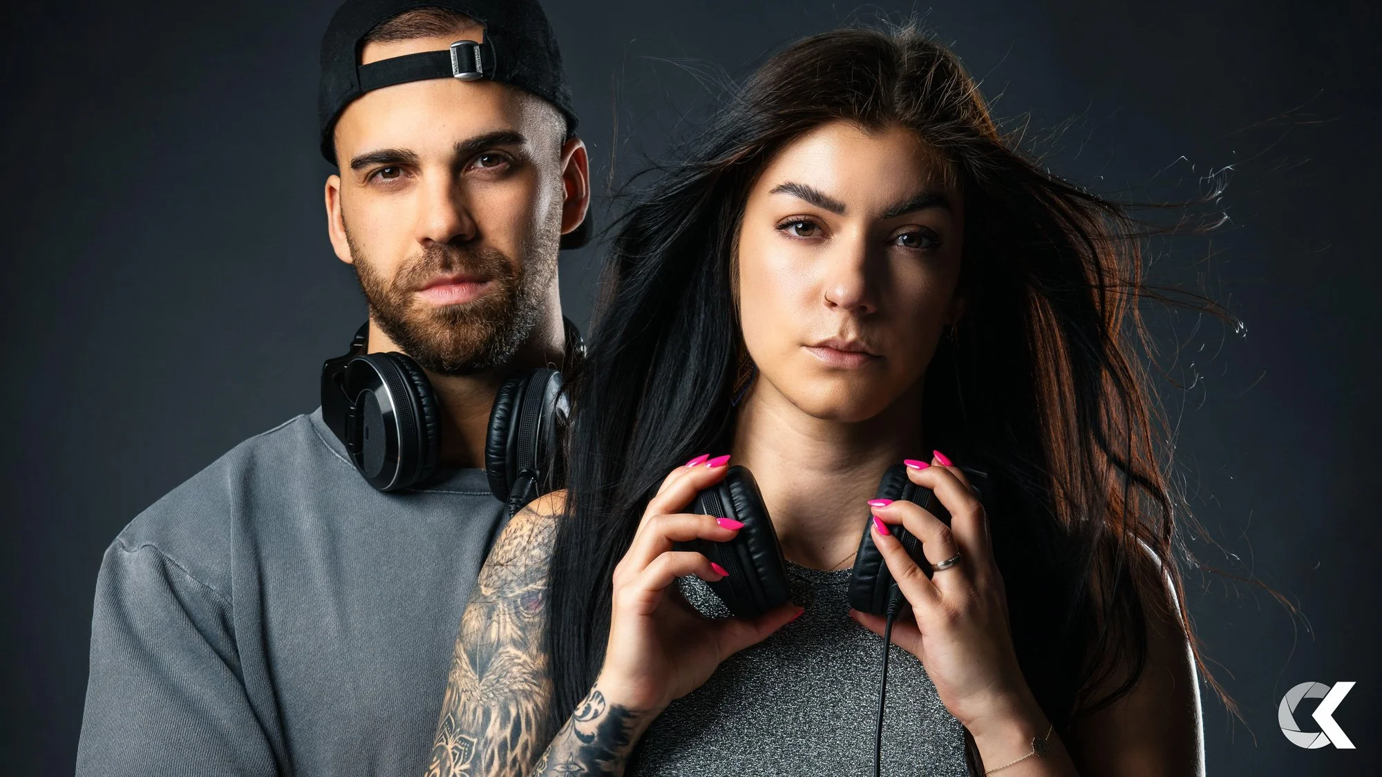 A man and a woman wearing headphones against a dark background.