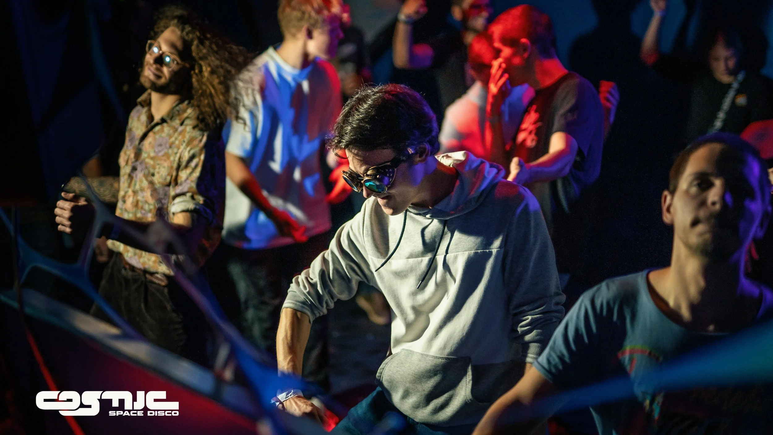 Young people dancing and enjoying themselves at a nightclub with colorful lighting and a dark background.