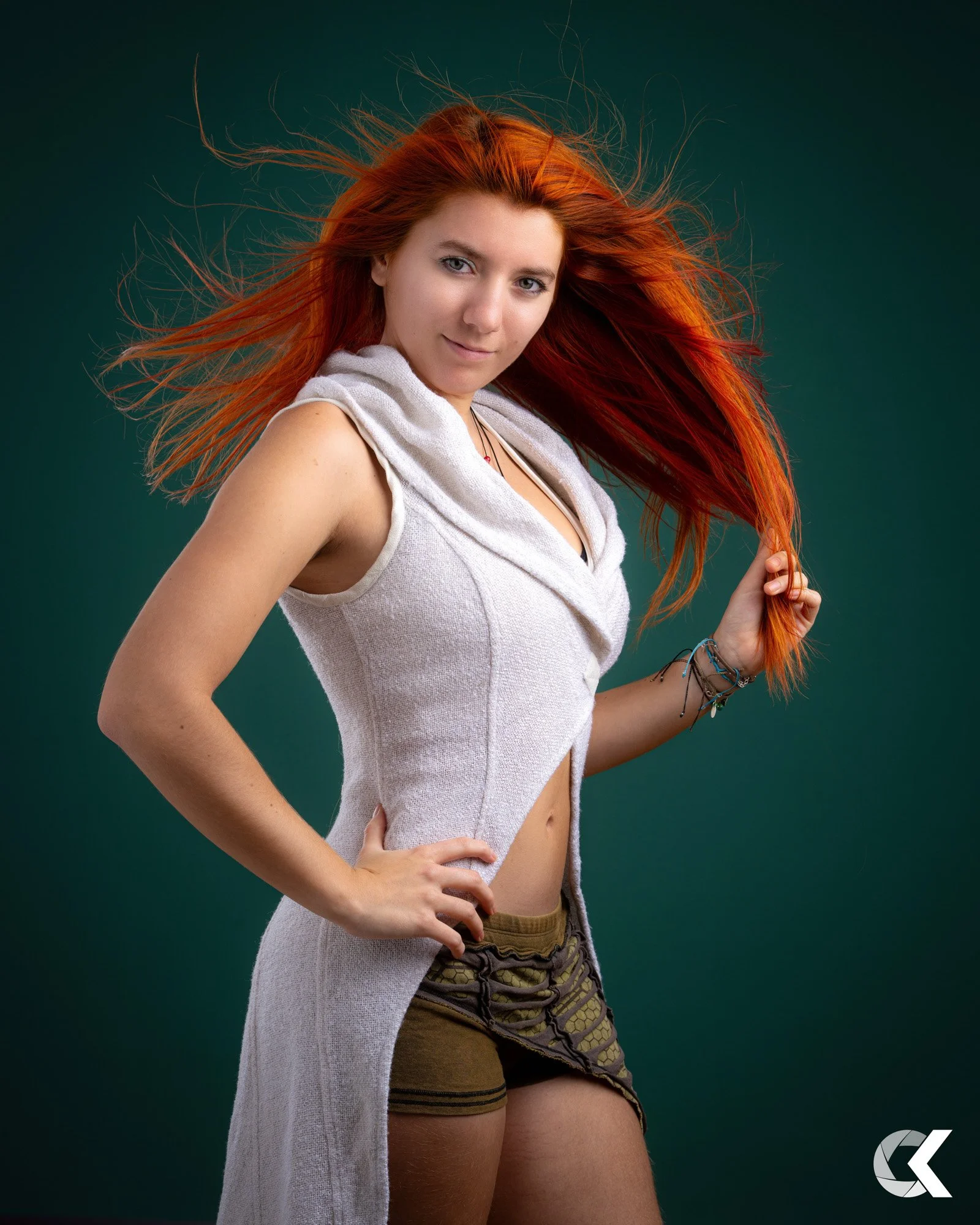 Junge Frau mit roten Haaren, die eine Hand auf die Hüfte stützt und die andere Hand in den Haaren hält, vor grünem Hintergrund