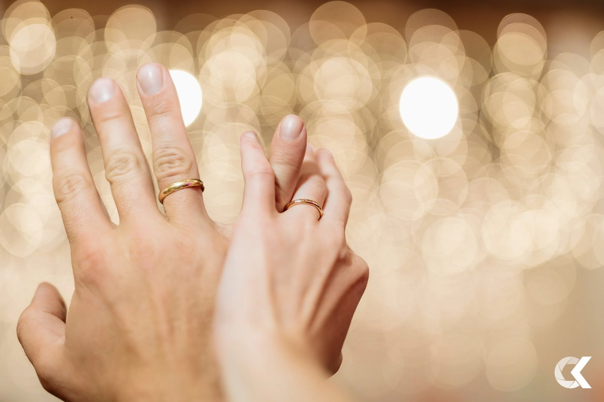 Two hands with wedding rings against a blurred, golden, bokeh background.