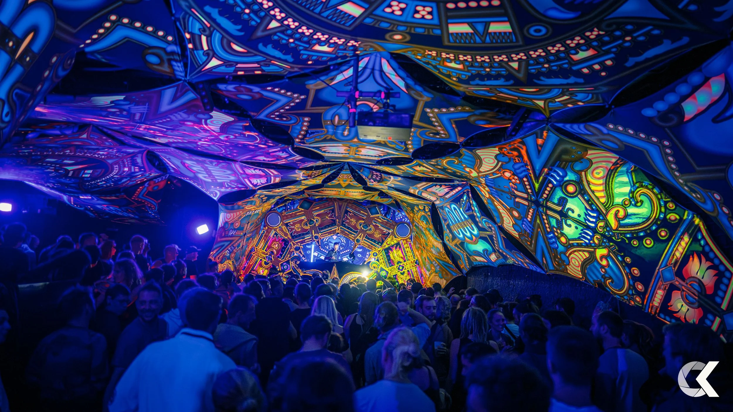 Crowd of people at a vibrant electronic music concert with neon artwork on the ceiling and walls.