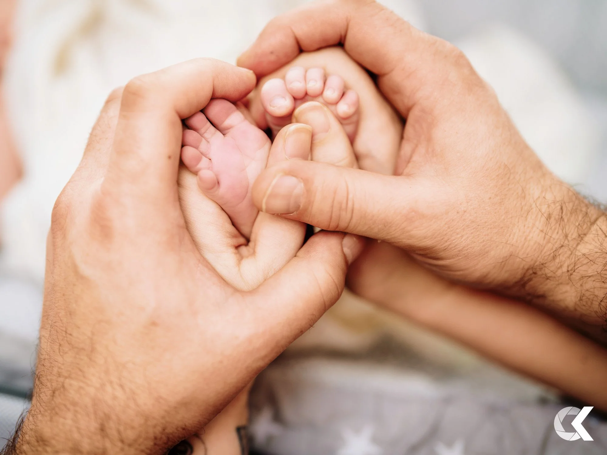 Close-up of adult hands holding tiny baby's feet and toes in a heart shape.