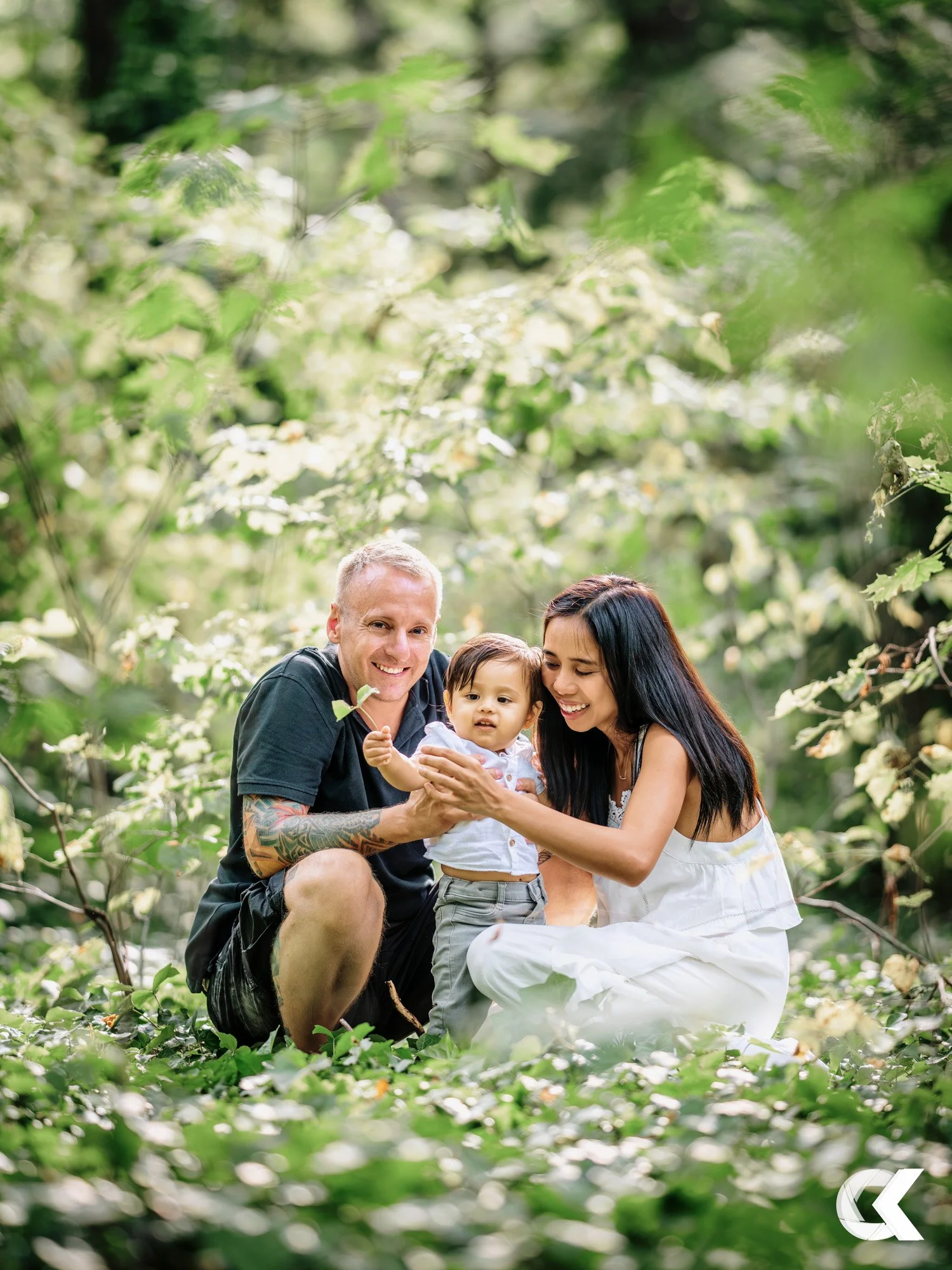A family of three, a man, a woman, and a young child, in a lush green outdoor setting, smiling and playing together.