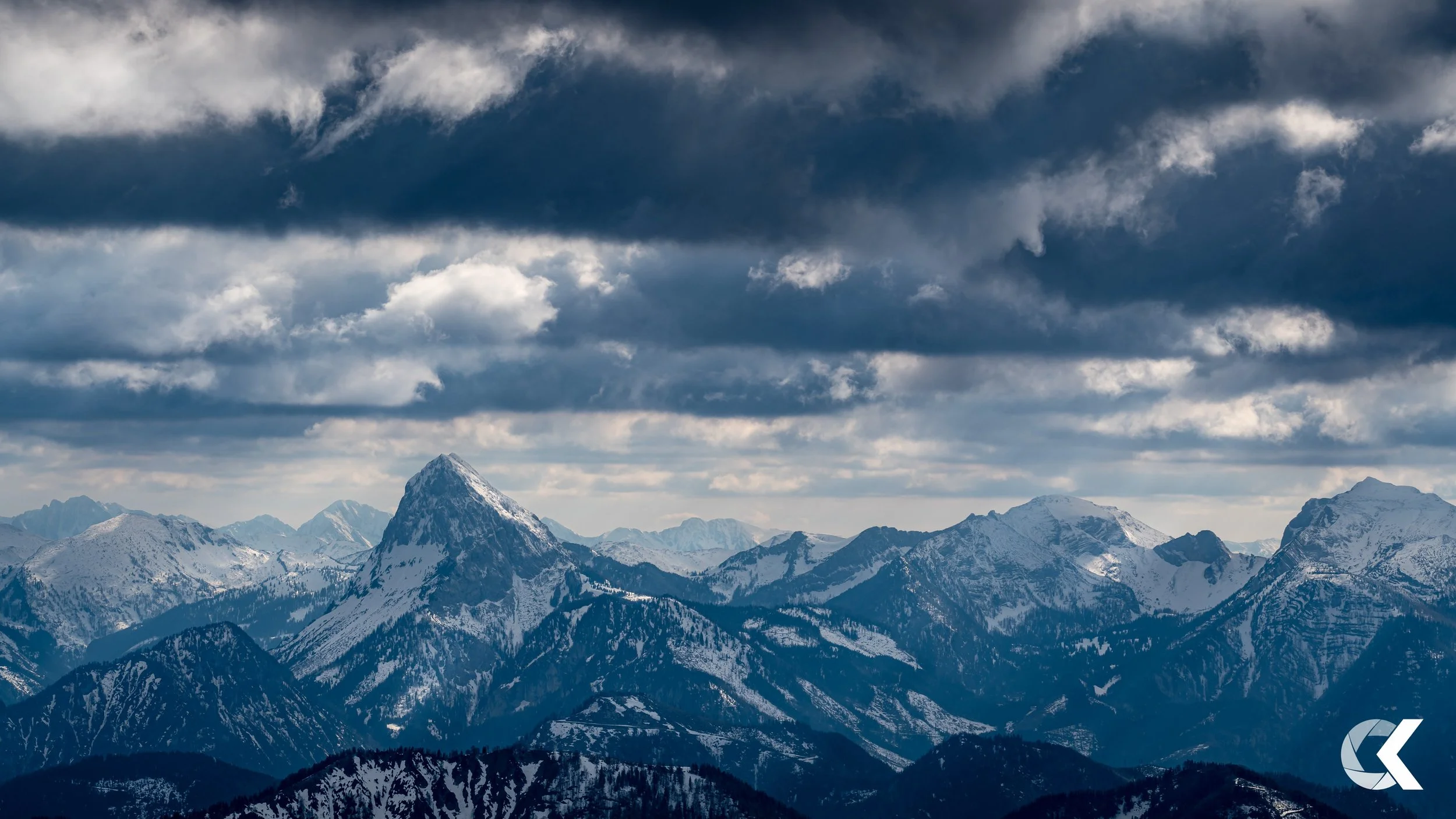 Snow-covered mountain range under dark, cloudy sky.