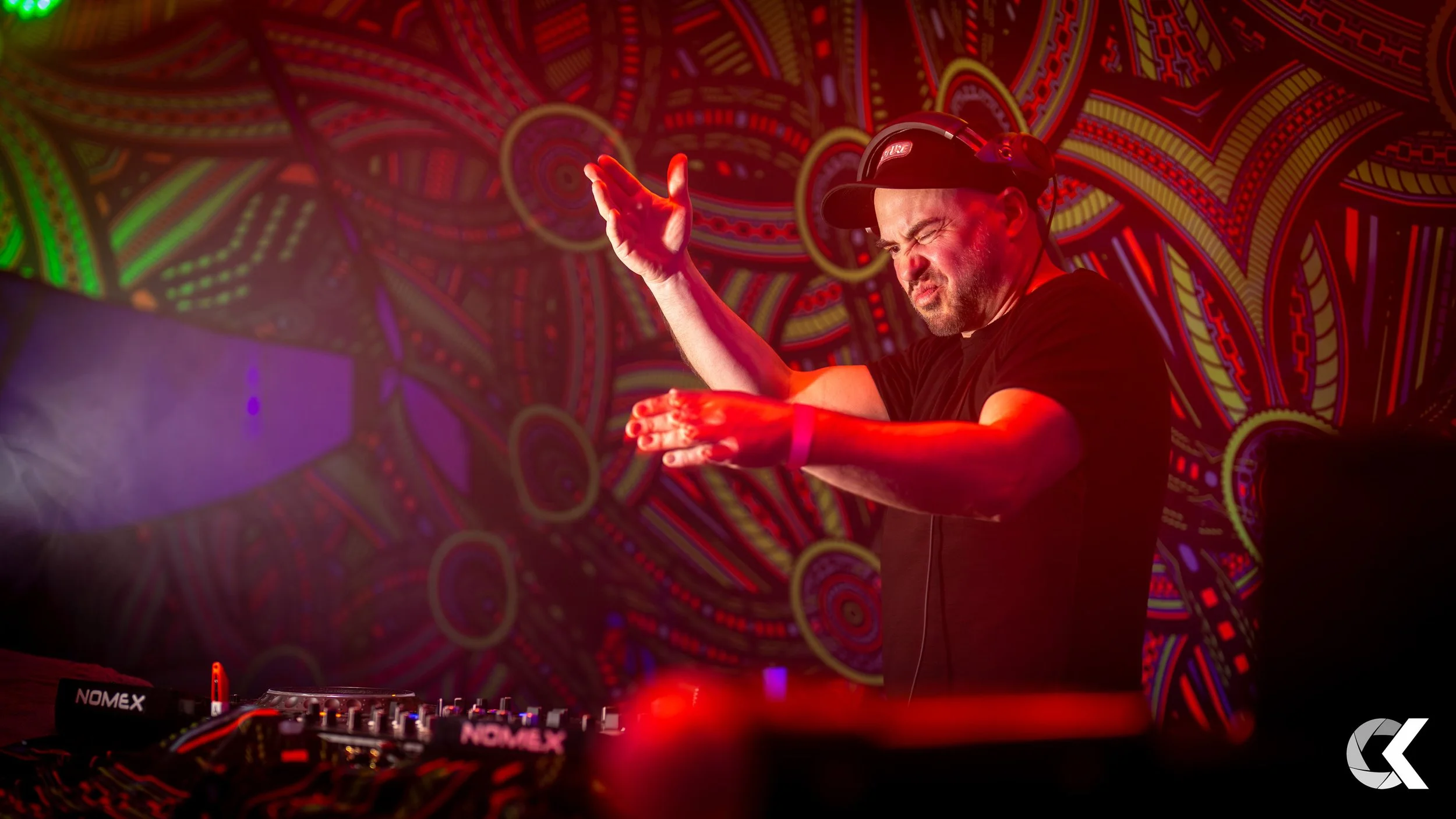 A DJ performing at a nightclub, with a colorful, patterned background and colorful lighting.
