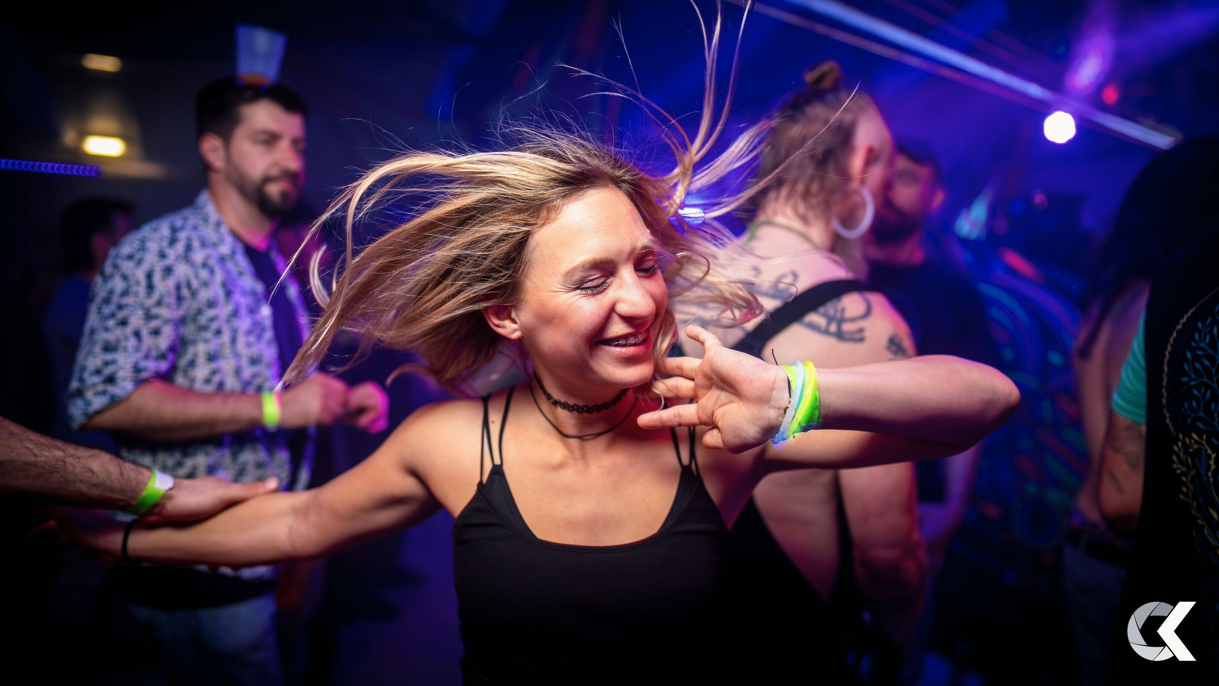 Woman dancing at a party with colorful lights, with other people in the background.