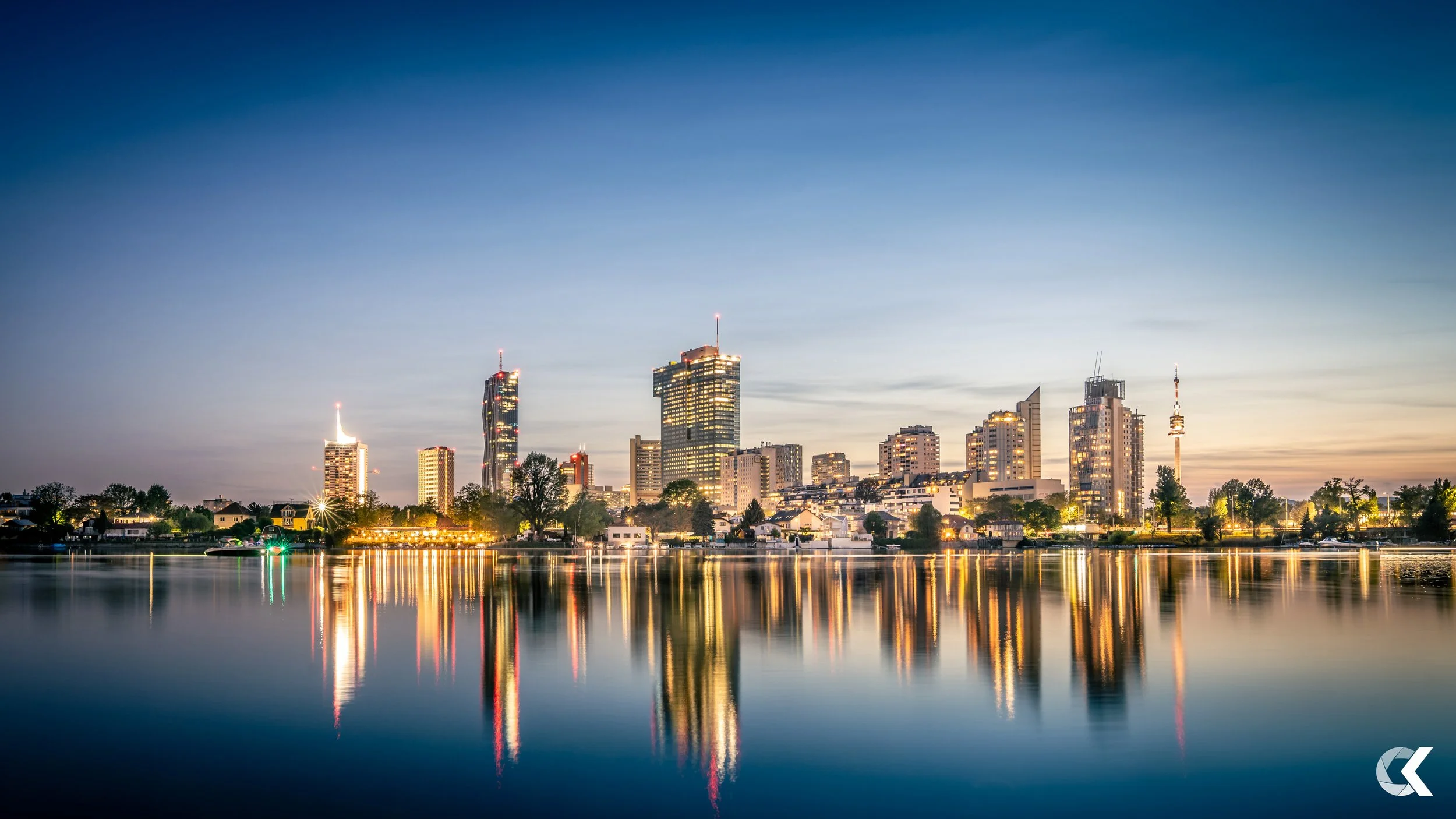 Downtown city skyline at dusk with buildings and their reflections in the calm water.