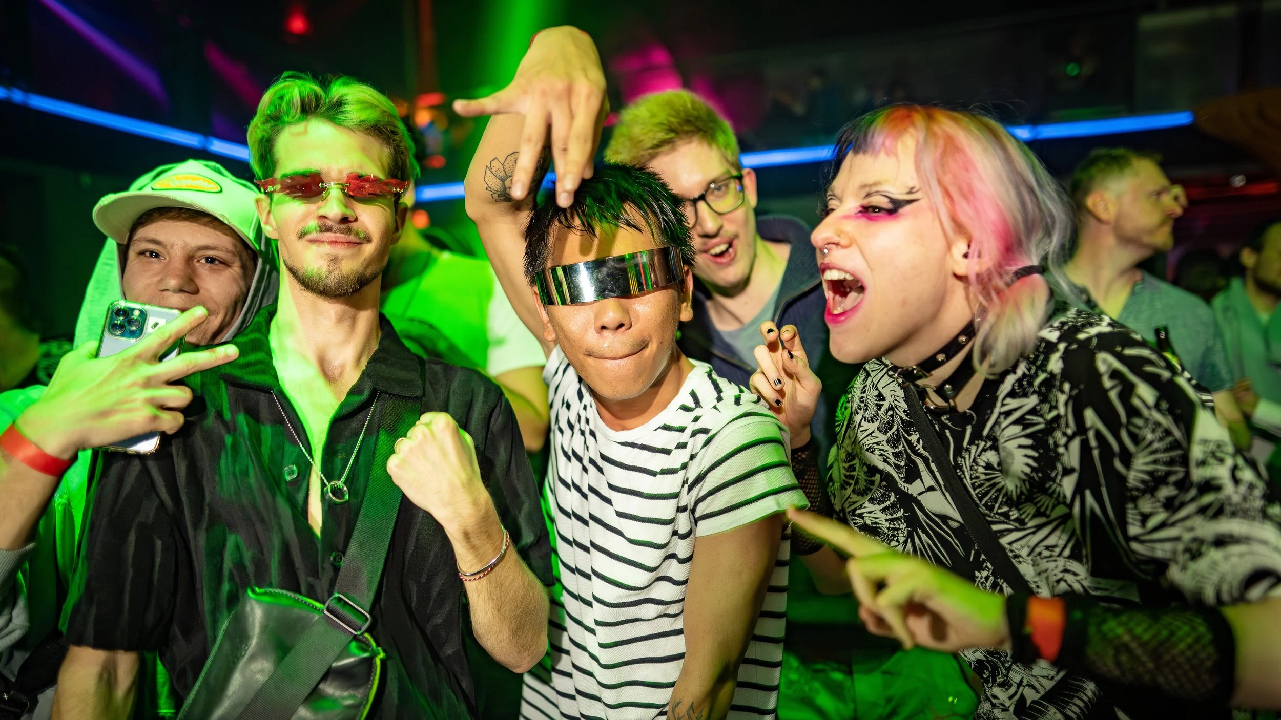 Group of young people at a party with colorful lights, wearing trendy clothing, and showing energetic poses and expressions.