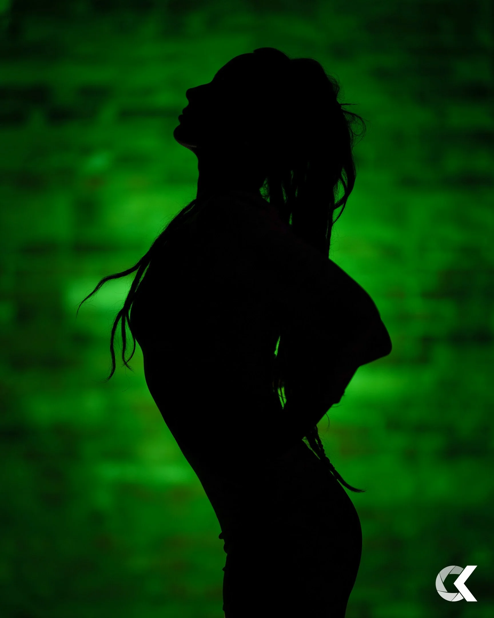 Silhouette of a woman with long hair, standing with her eyes closed against a green background.