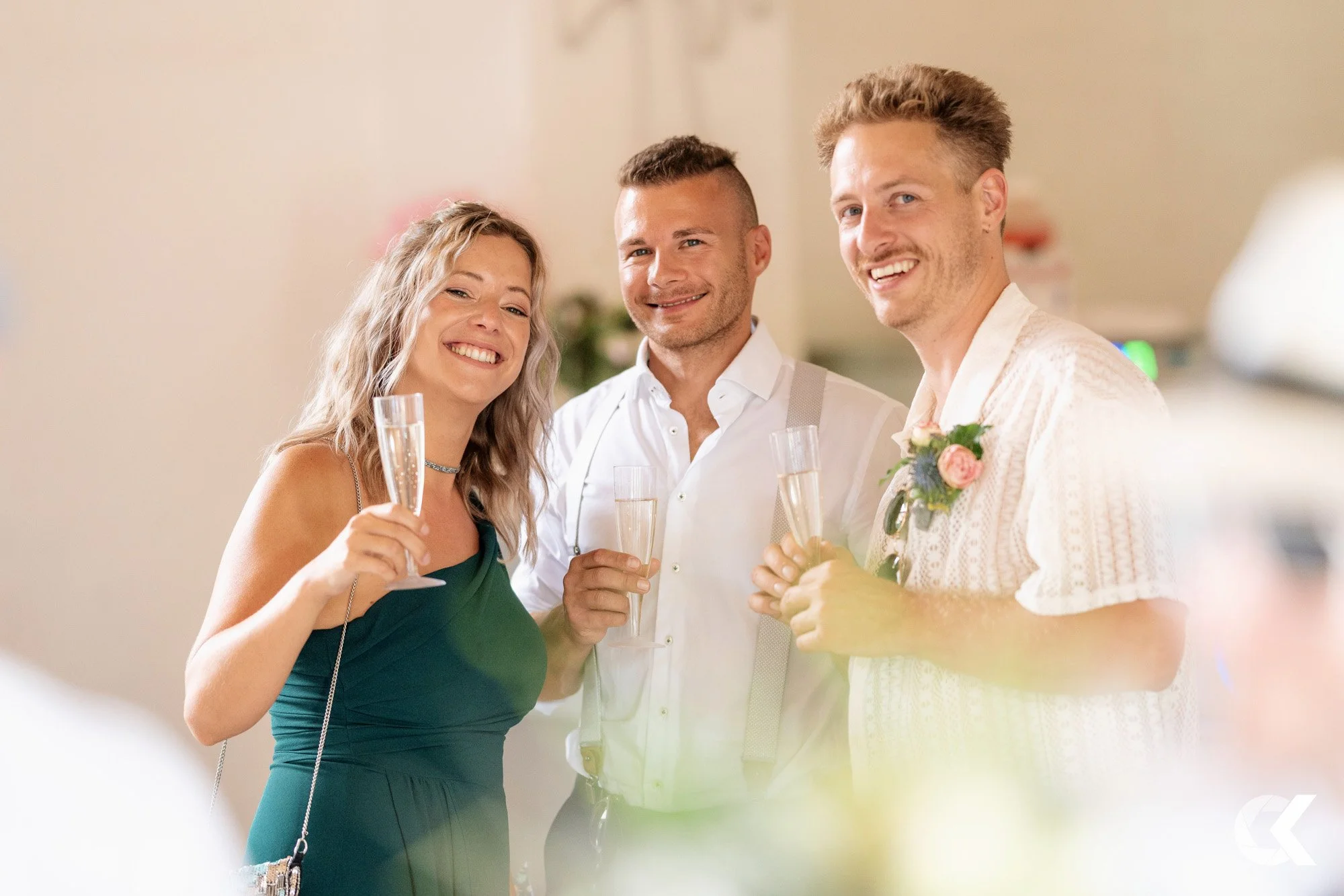 Three friends celebrating at a party, smiling and holding champagne glasses, in a softly lit indoor setting.