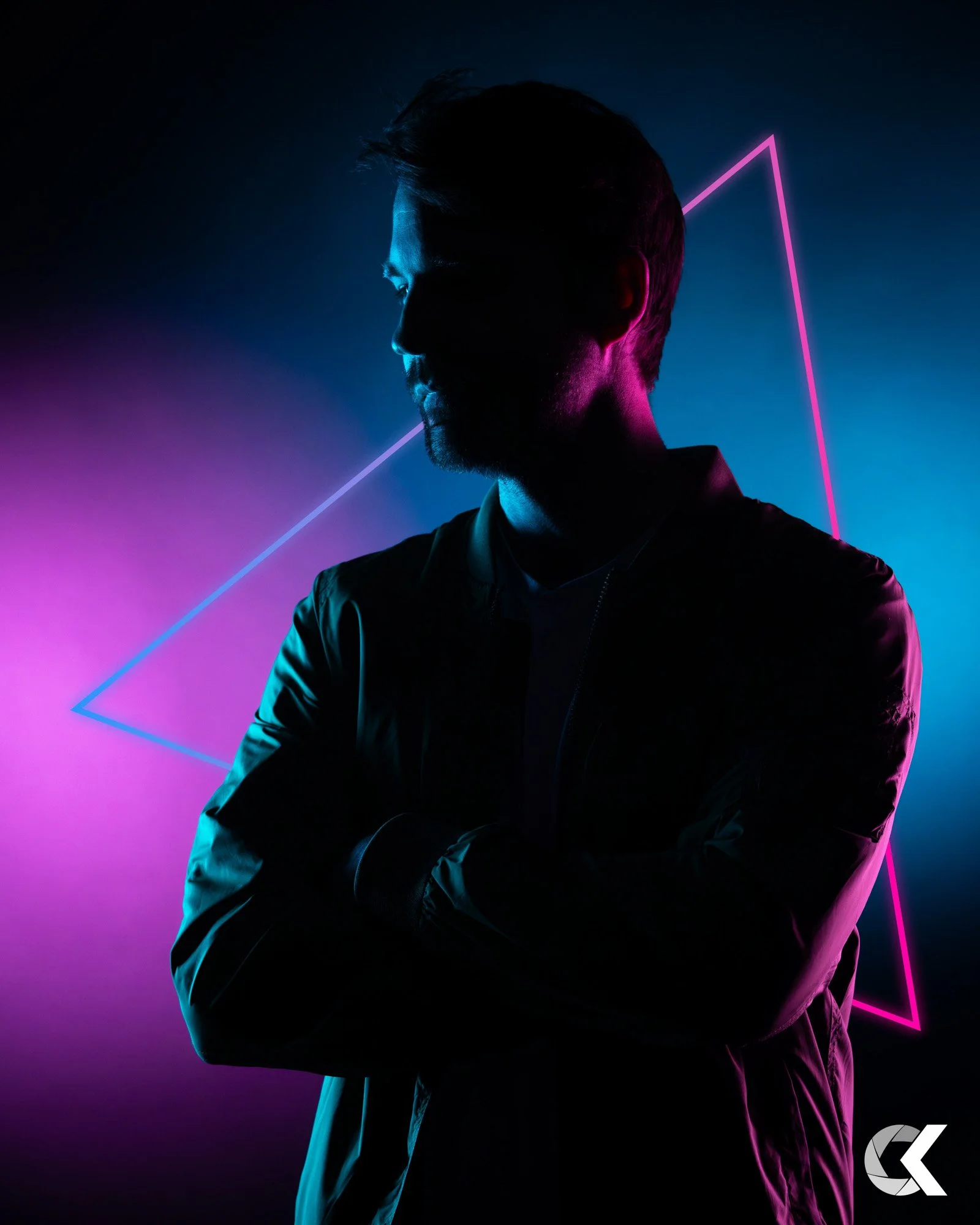 Silhouette of a man with crossed arms in front of a neon pink and blue geometric background.