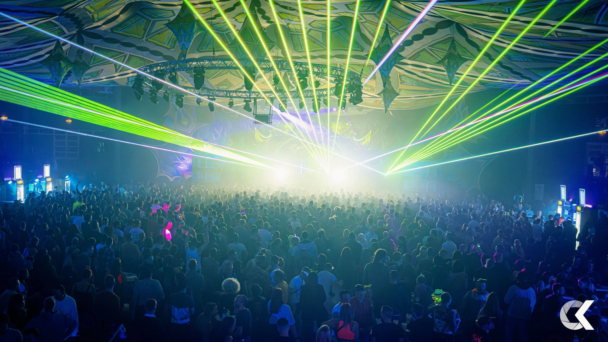 Crowd of people at a concert or rave with laser lights and colorful stage lighting.
