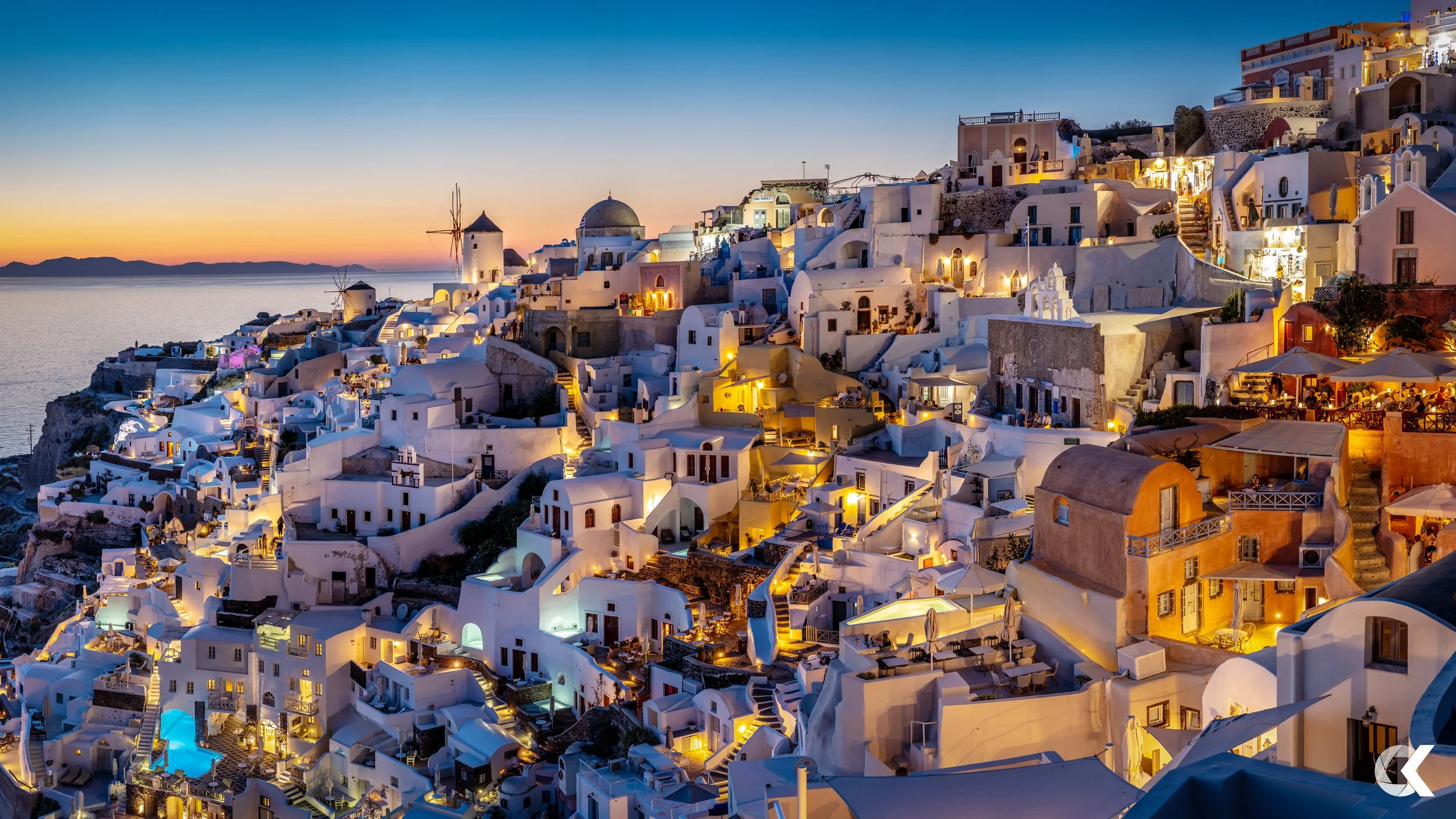 View of Santorini's white-washed buildings and churches illuminated at sunset with the calm sea in the background.