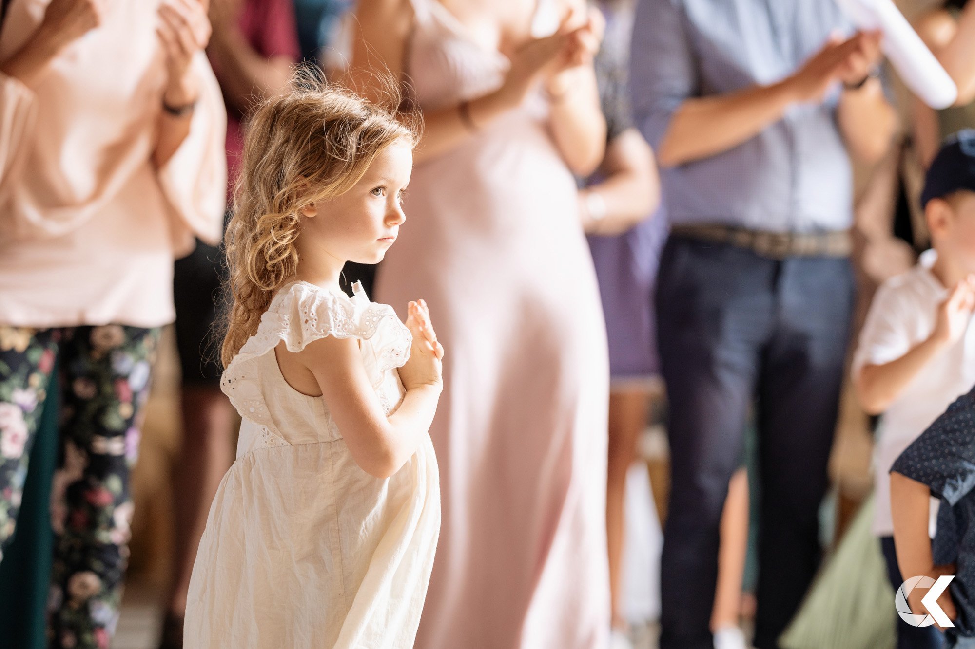 A young girl standing in a crowd, with her hand over her heart during what appears to be a ceremony, with adults around her also participating.