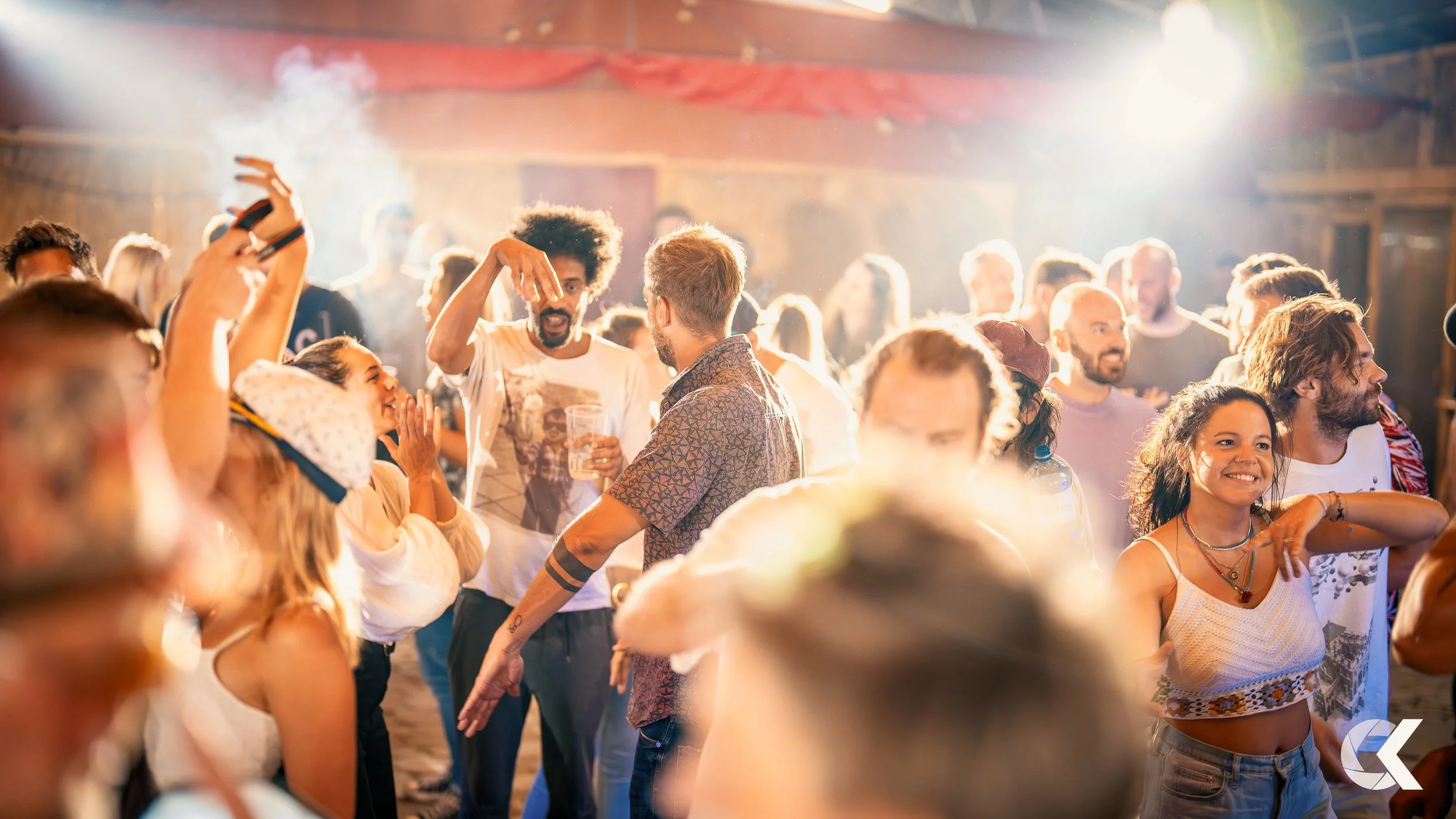 People dancing and socializing at a lively indoor party with bright lighting and a smoky atmosphere.