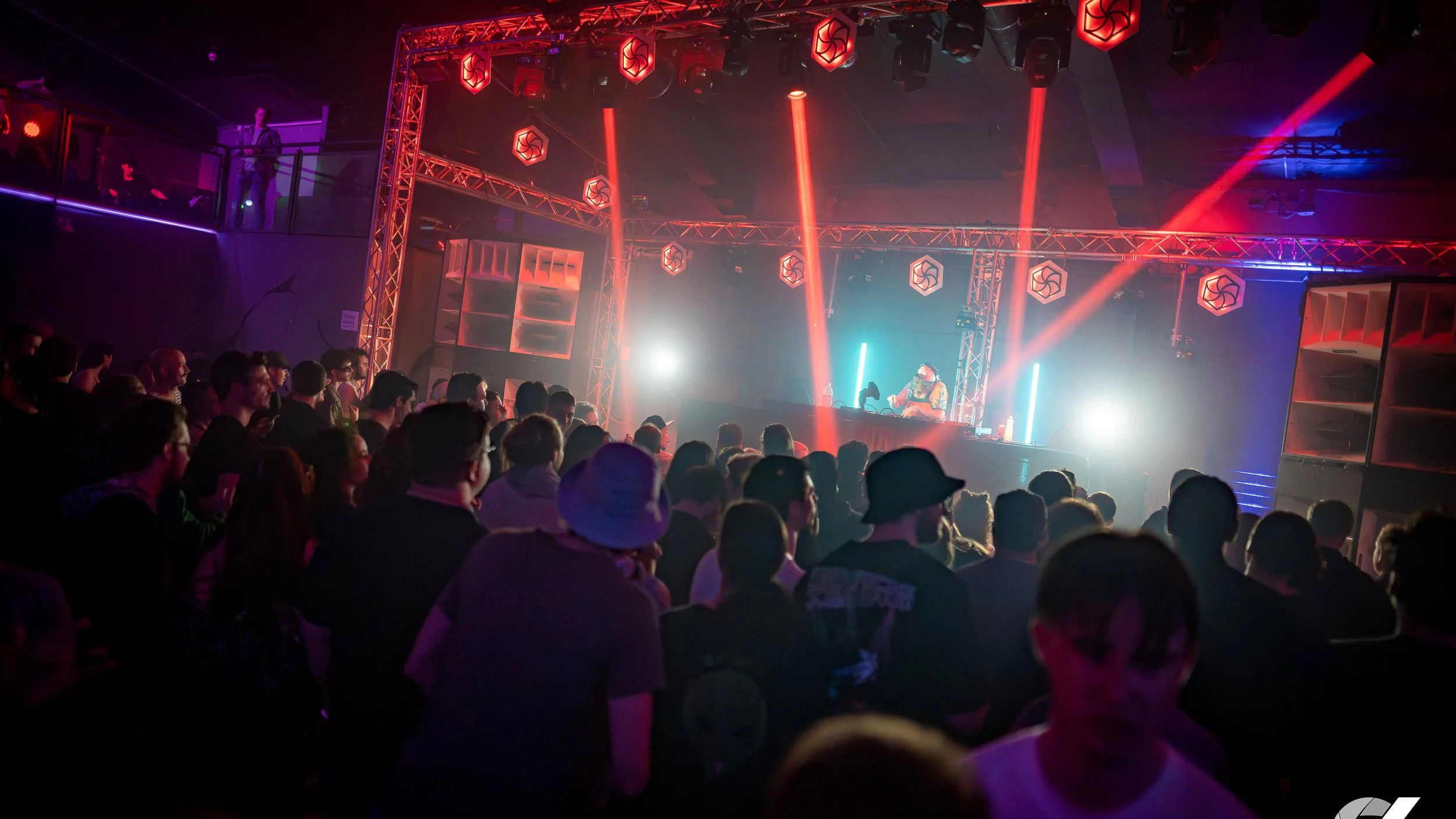 Crowd of people watching a DJ perform at a concert with colorful stage lighting and geometric decorations.