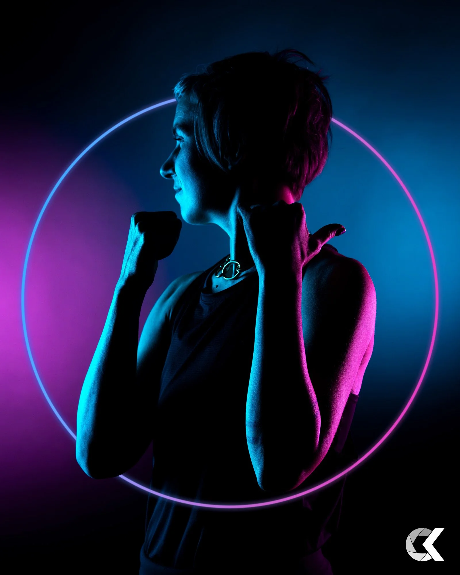 Seitliche Silhouette einer jungen Frau mit kurzen Haaren, die in Neonblau und -pink beleuchtet ist, vor einem dunklen Hintergrund mit einer leuchtenden kreisförmigen Lichtlinie.