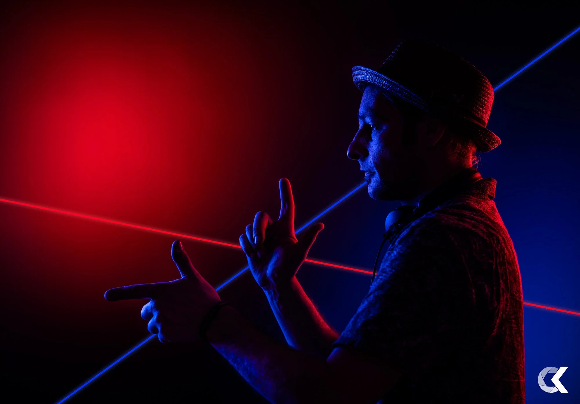 Ein Mann trägt einen Hut und benutzt Kopfhörer, während er in Neonlichtern in Rot und Blau posiert.