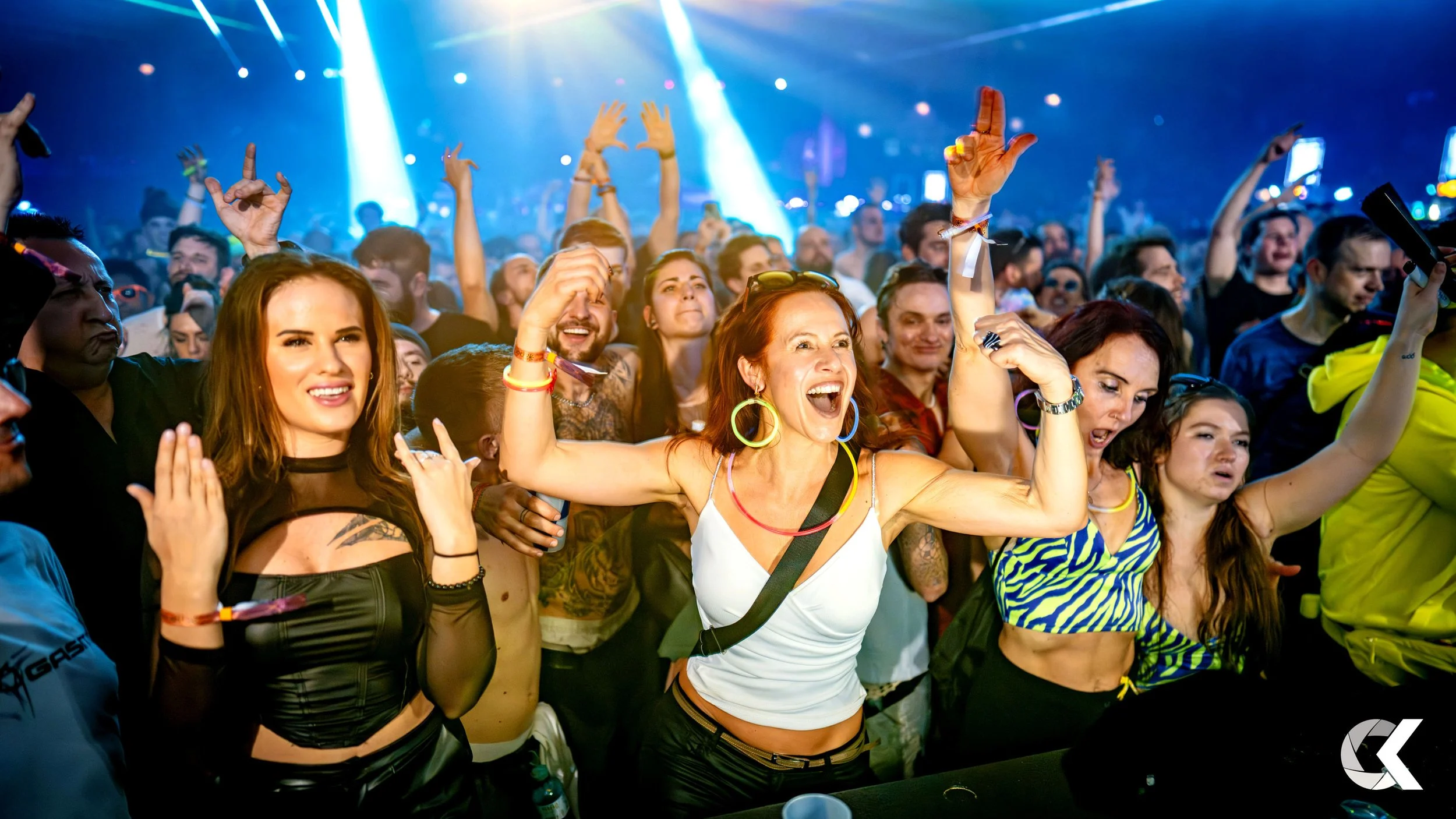 Crowd of concert-goers dancing and cheering under bright blue stage lights.