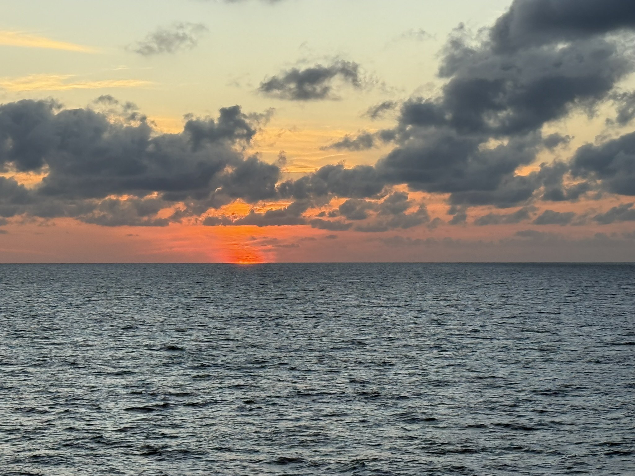 sunset over the ocean with clouds in the sky.