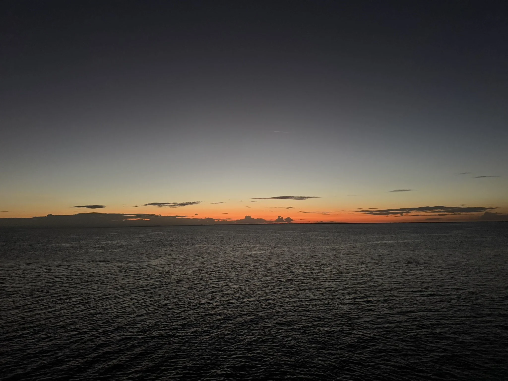 Sunset over the ocean with a clear, darkening sky and a few scattered clouds near the horizon.