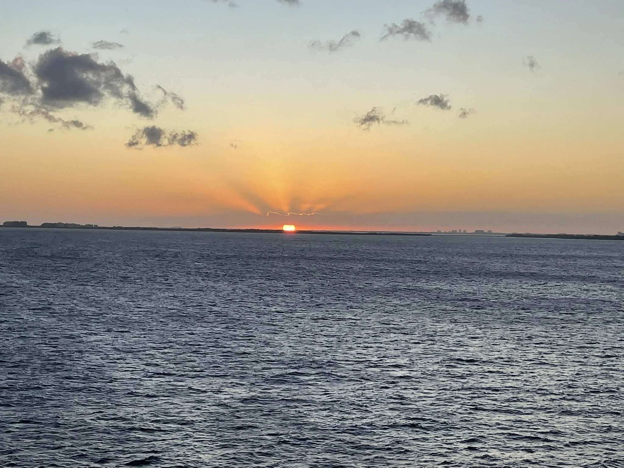 Sunset over the ocean with rays of sunlight and scattered clouds in the sky.