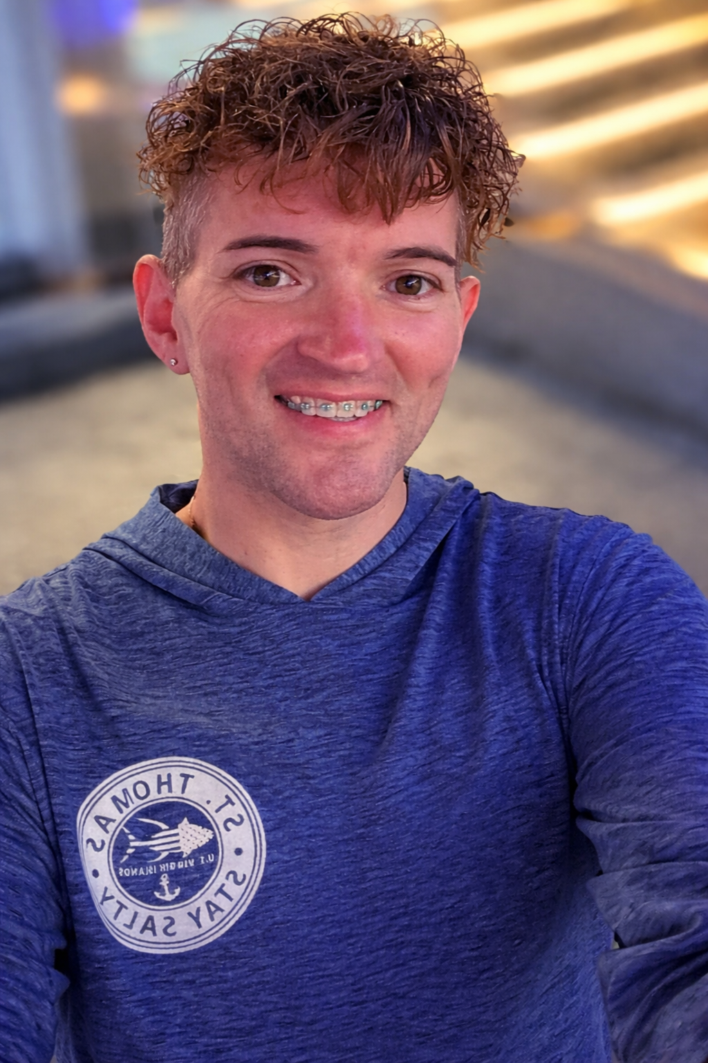 Young man with curly brown hair smiling, wearing braces and a blue hoodie with a logo that reads 'St. Andrew's Stay Salty'.