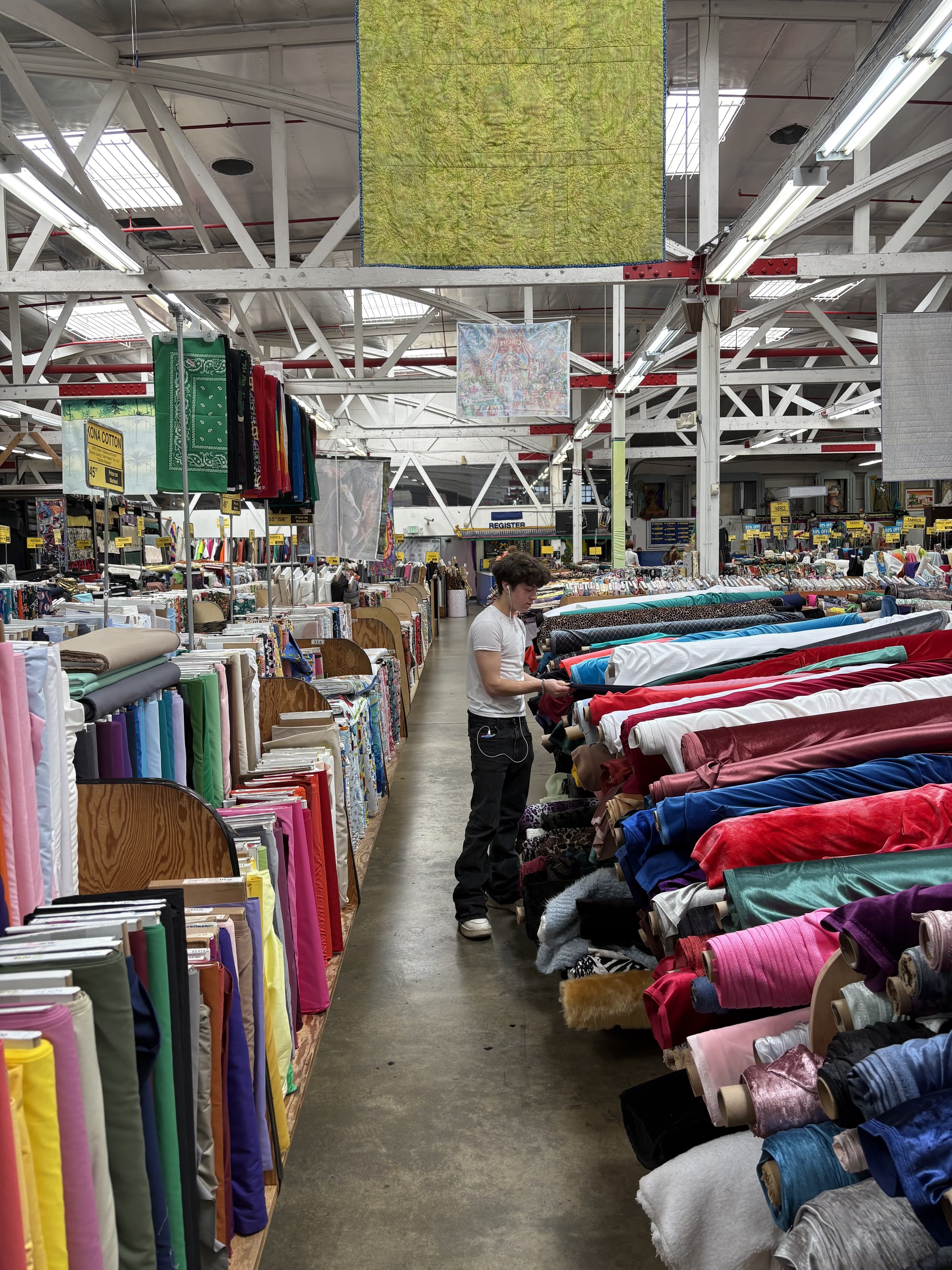 Inside a fabric store or textile market with colorful rolls of fabric on shelves and a person shopping.
