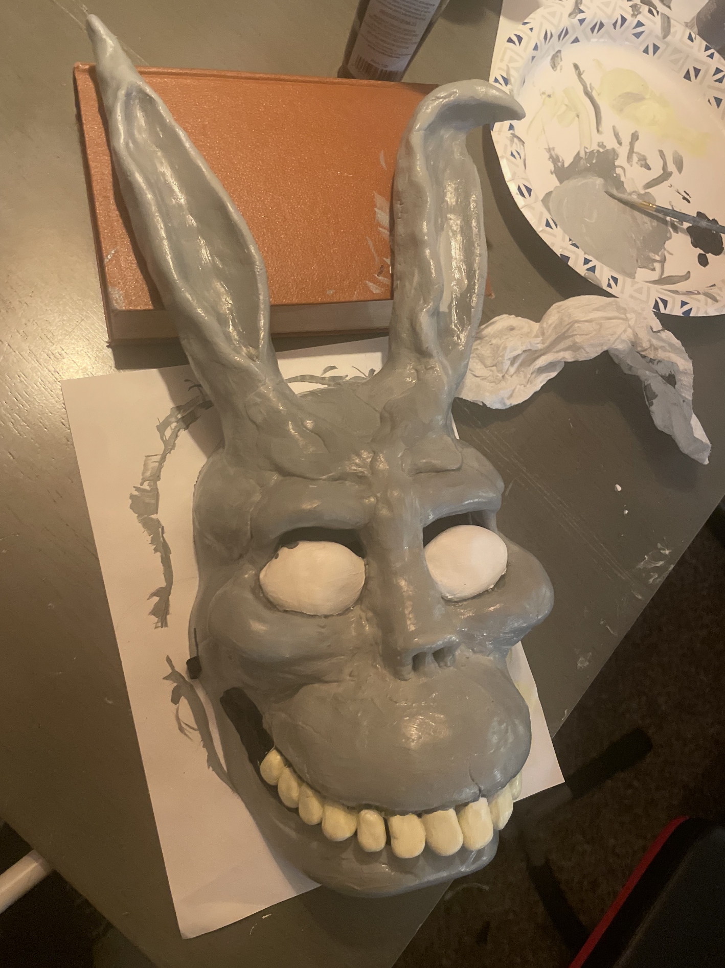 A sculpted face of a skull with a prominent forehead, deep eye sockets, and a row of teeth. The skull is painted in shades of gray.
