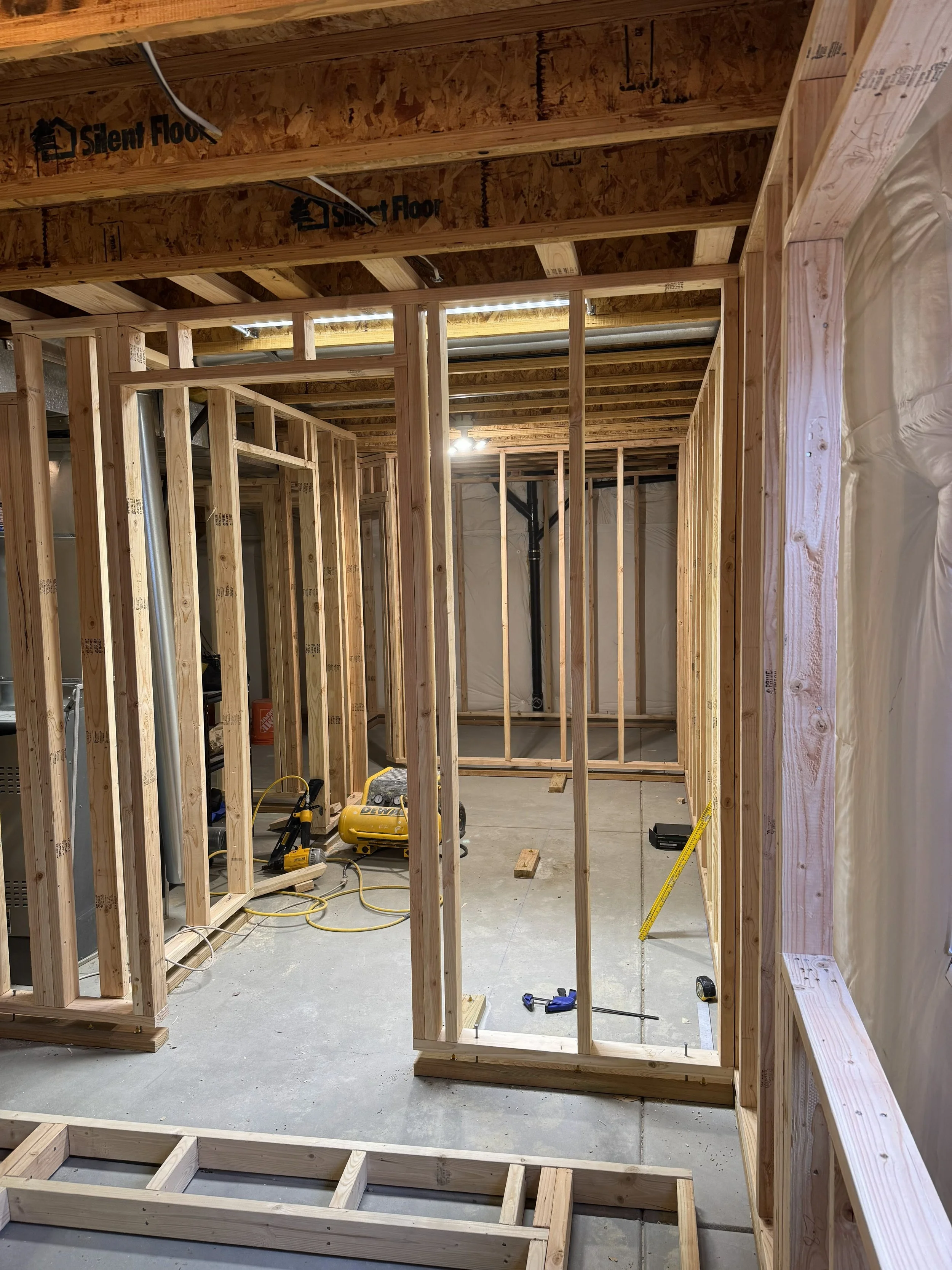 Interior of a house under construction with exposed wooden framing, construction tools, and equipment on the concrete floor