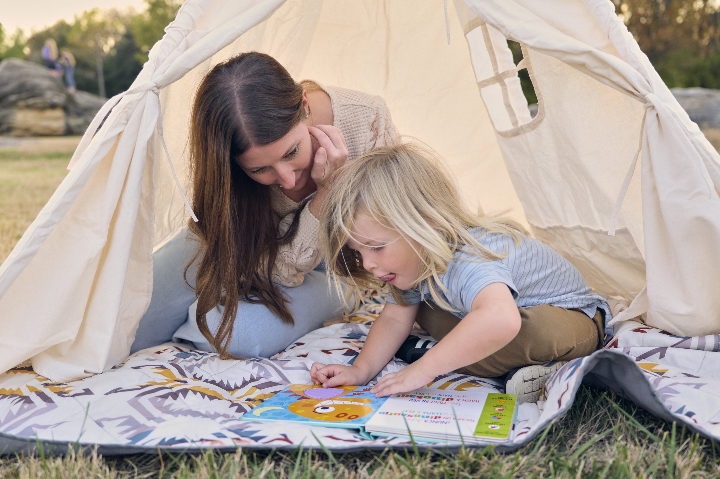 A BCBA and autistic boy inside a fabric tent outdoors, playing in a natural environment.