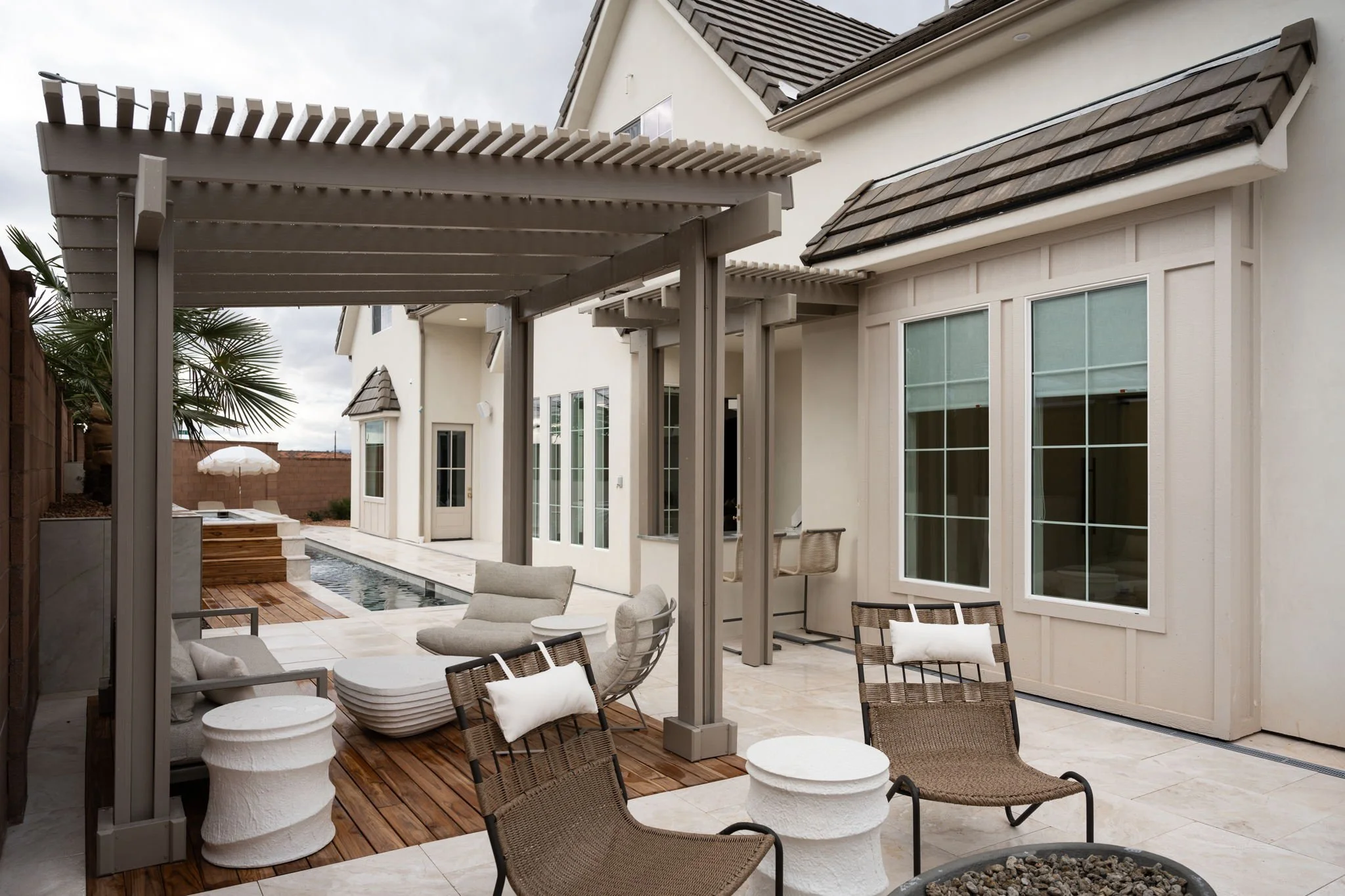 Modern backyard patio featuring a pergola, outdoor seating, large windows, a small pool, and a tiled floor.