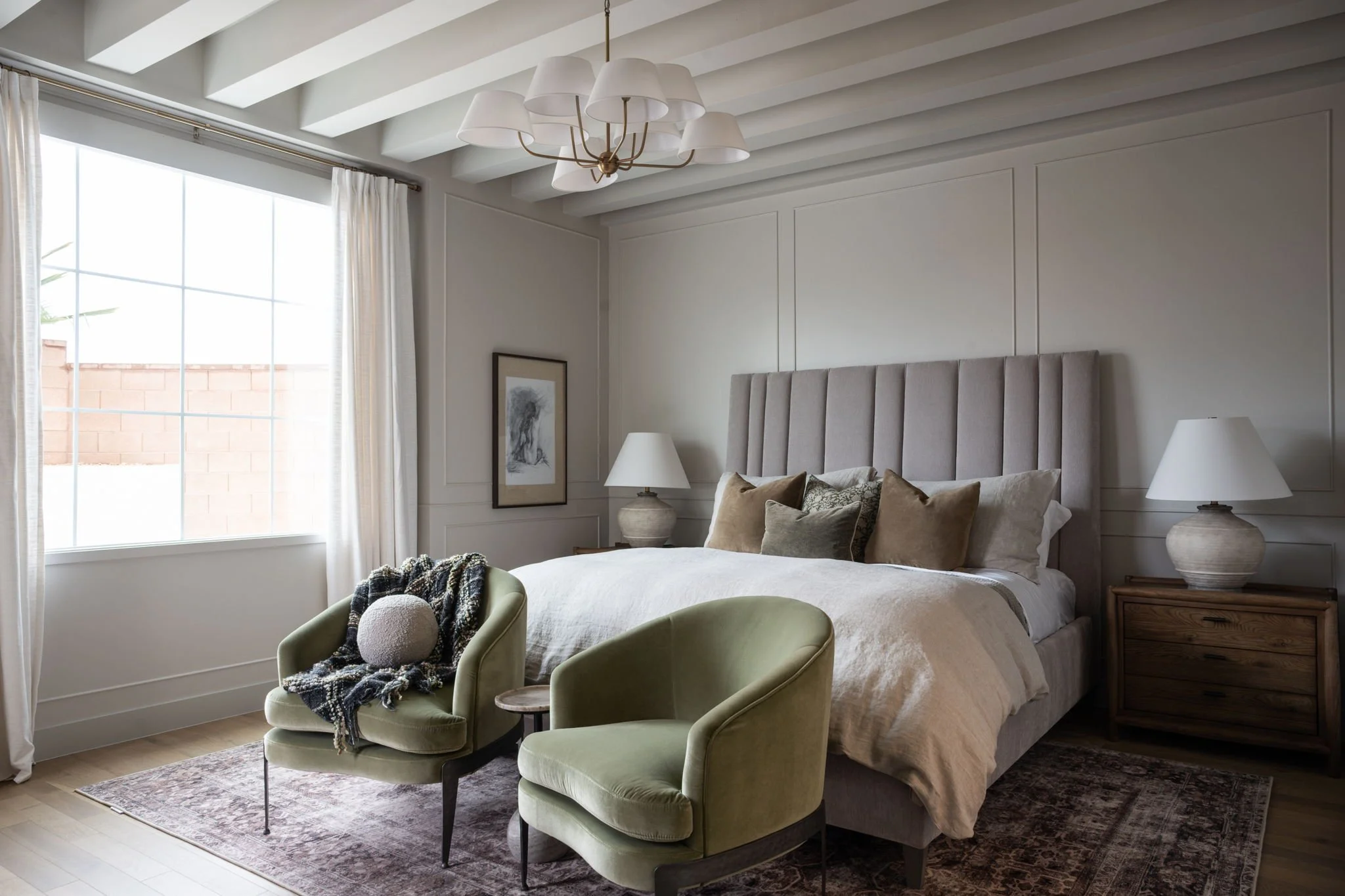 A bedroom with a large bed, green armchairs, side tables with lamps, and a window with white curtains.